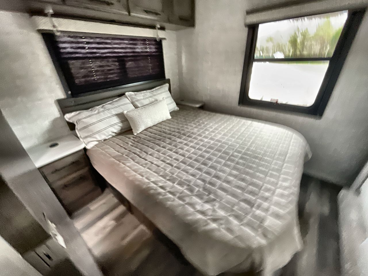 Cozy RV rental bedroom with a comfy bed, headboard, nightstands, and windows showing outdoor views.. Entegra Odyssey 2025