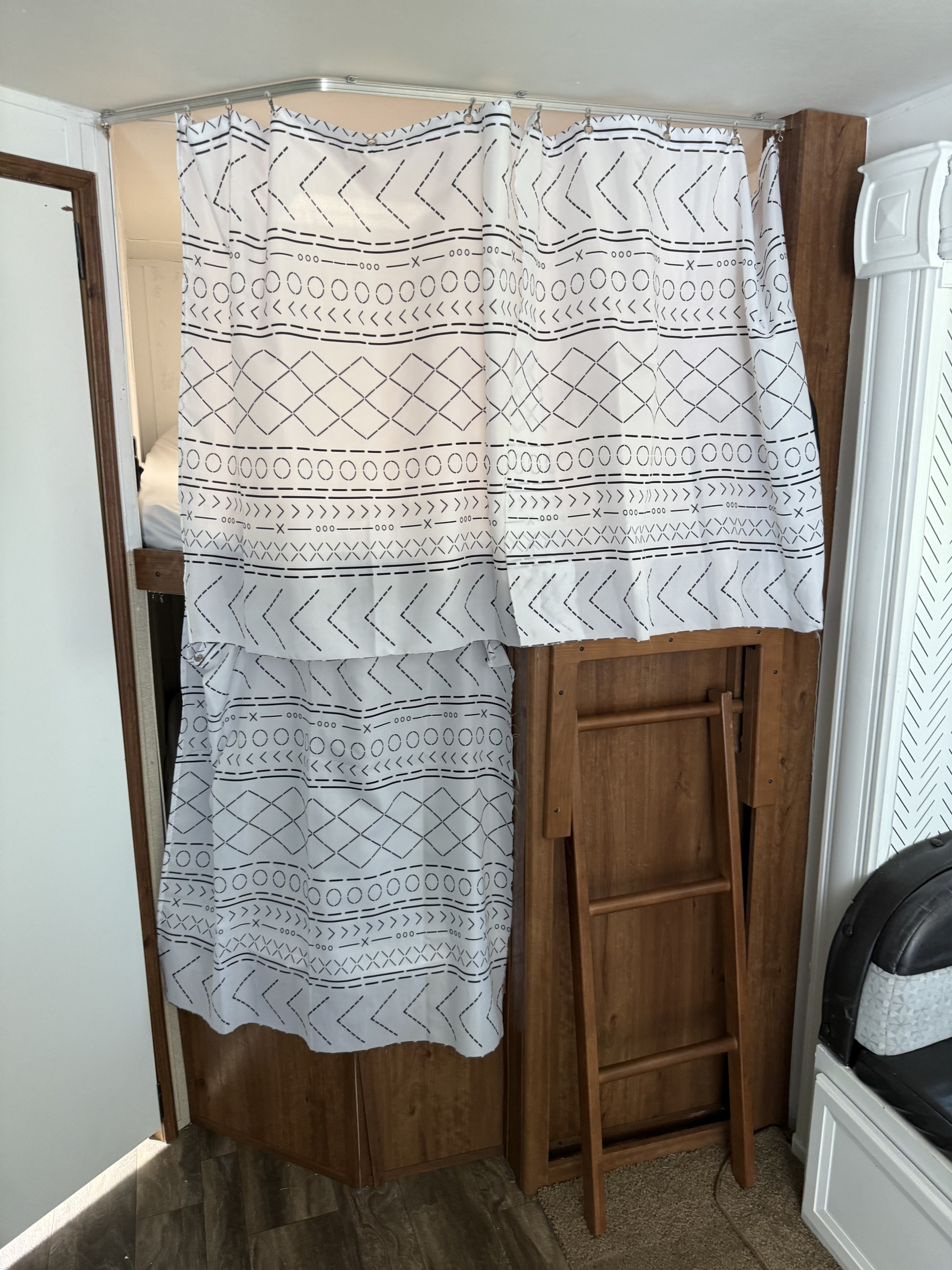 RV rental bunk area with a white and black patterned privacy curtain on a curved track, and a wooden ladder for access.. Gulf Stream Conquest 2016