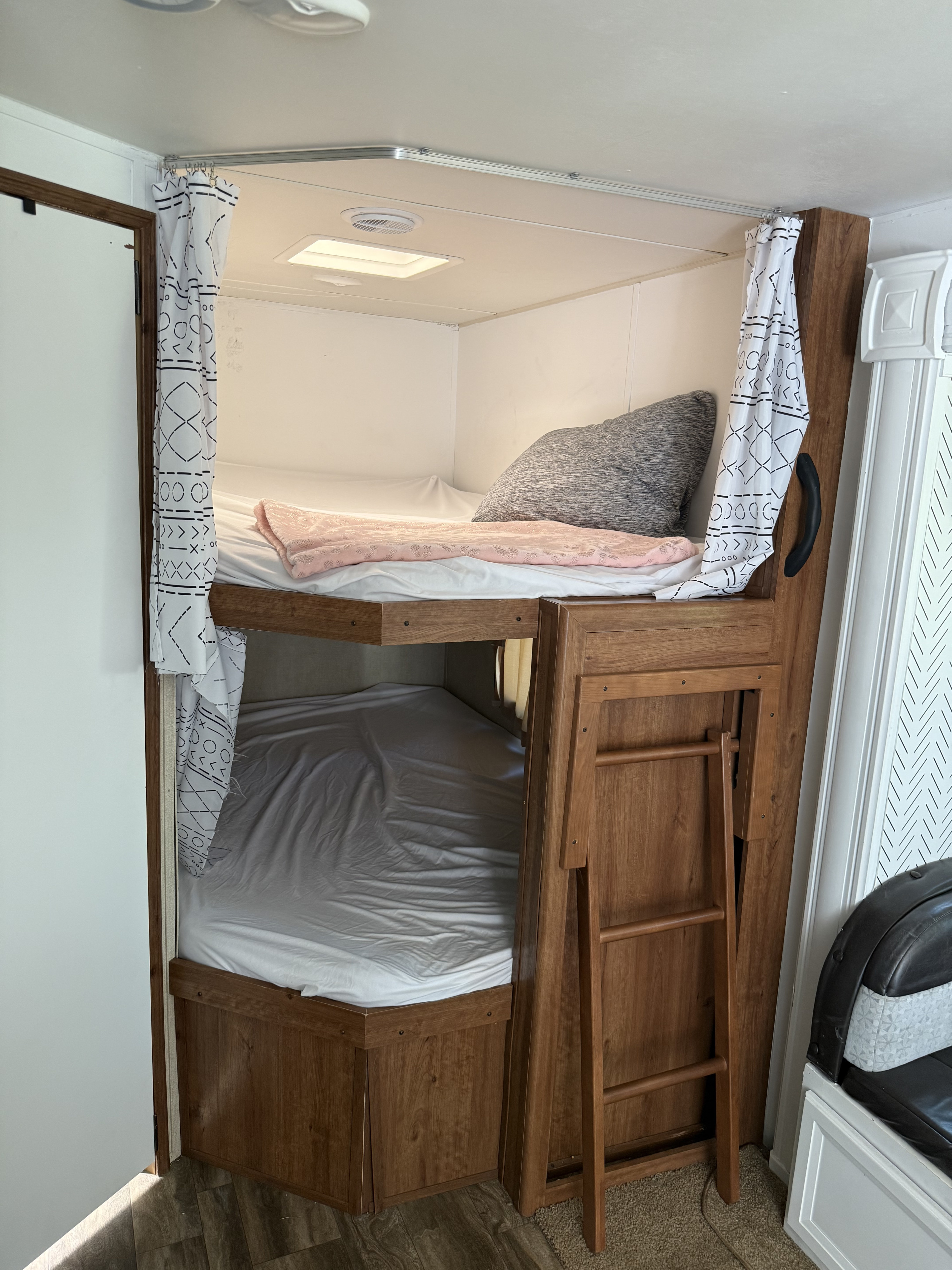 Inside an RV rental: Two cozy bunk beds with privacy curtains, a gray pillow, a pink blanket, and an accessible wooden ladder.. Gulf Stream Conquest 2016
