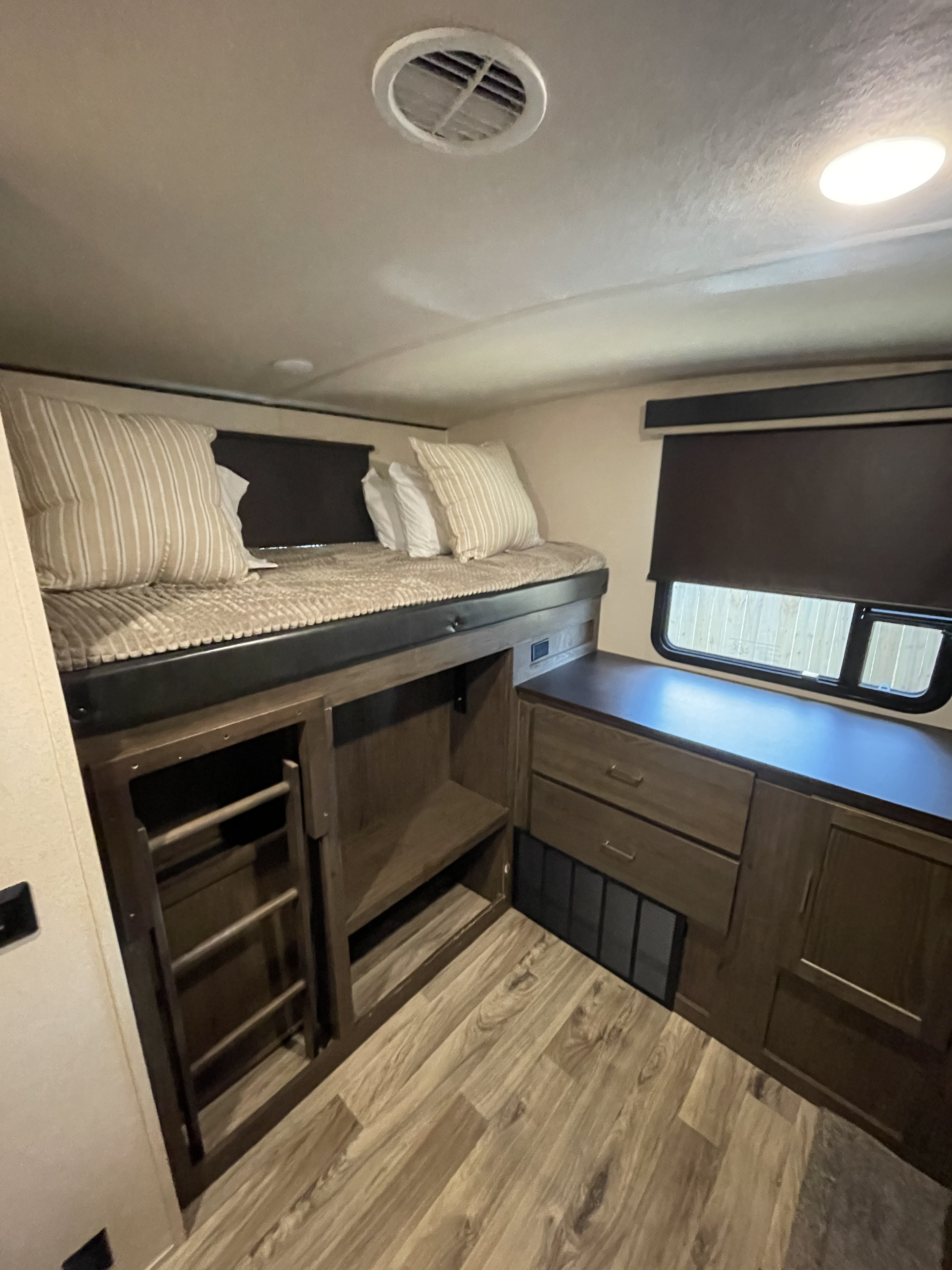 Cozy RV rental interior with a bunk bed, striped pillows, under-bed storage, drawers, and wood-look flooring.. Forest River Wildwood Heritage Glen LTZ 2019