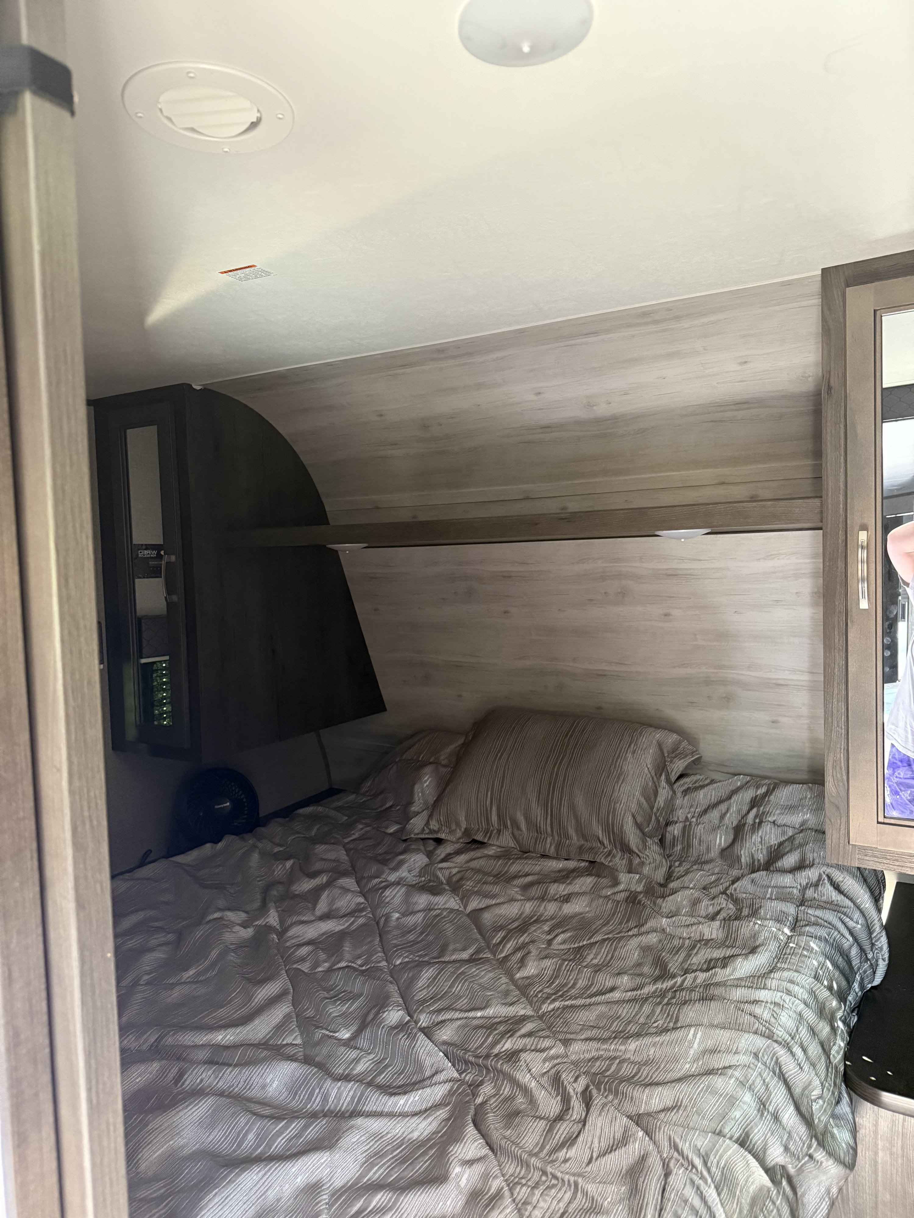 Inside an RV rental: a compact bedroom featuring a comfortable bed with textured gray bedding, fan, and storage cabinet.. Jayco Jay Flight 2022