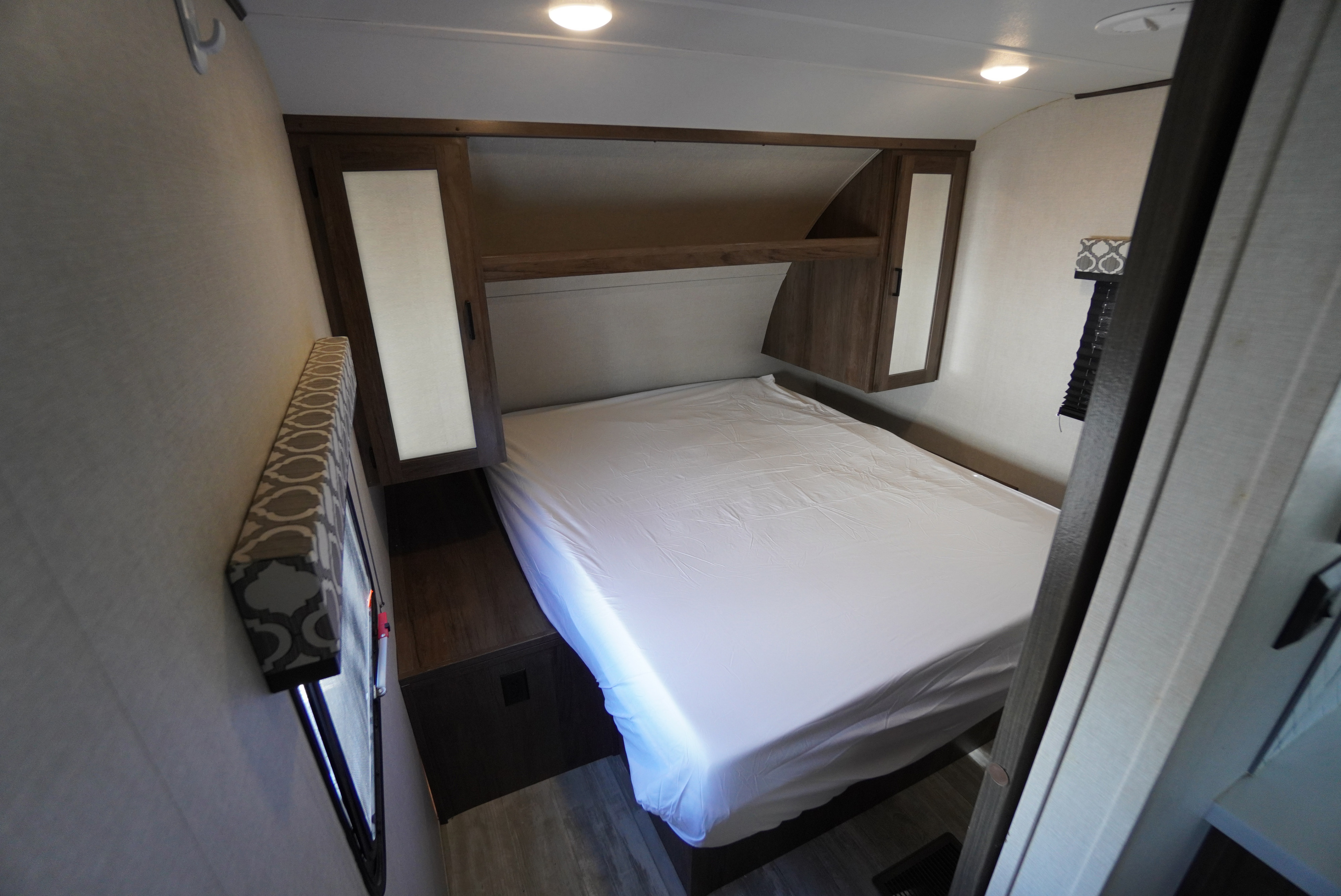View of a bright, modern RV rental bedroom with a neatly made bed, overhead storage, and integrated lighting.. Forest River Tracer 2021