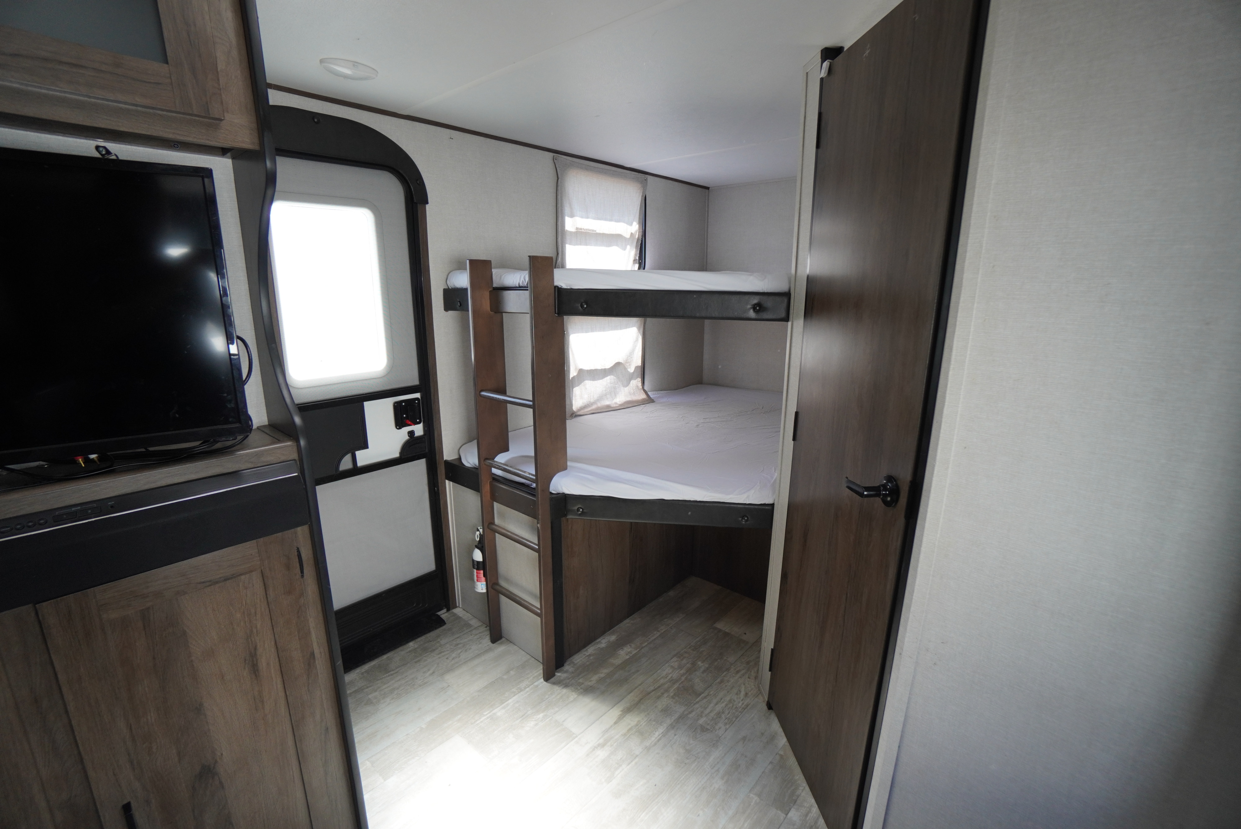RV rental interior: View of modern bunk beds, TV entertainment center, and an entry door, providing cozy accommodations.. Forest River Tracer 2021