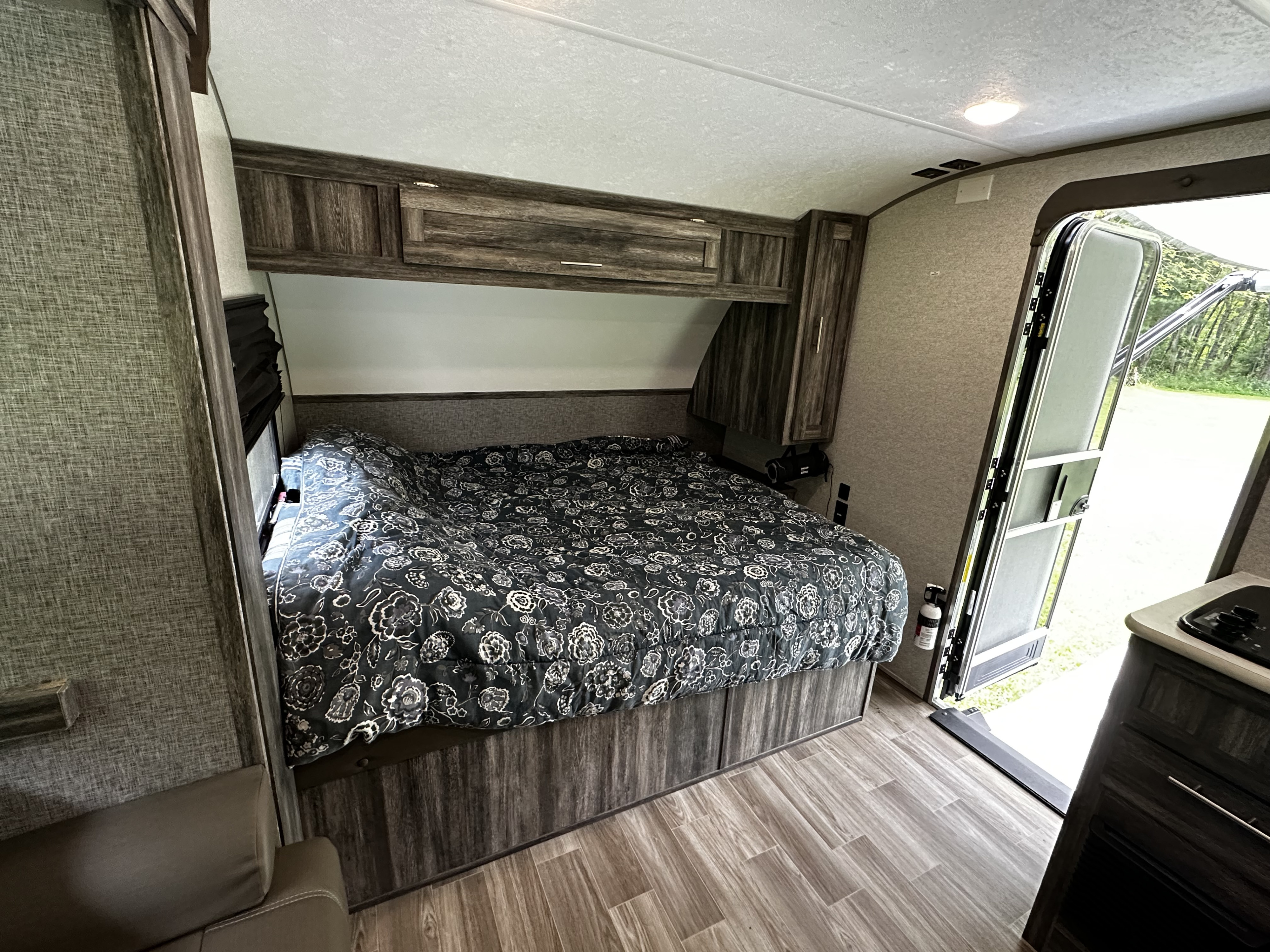 Step into this spacious RV rental interior! Features a cozy bed, overhead cabinets, a compact kitchen, and an open door to nature.. Forest River Salem FSX 2020