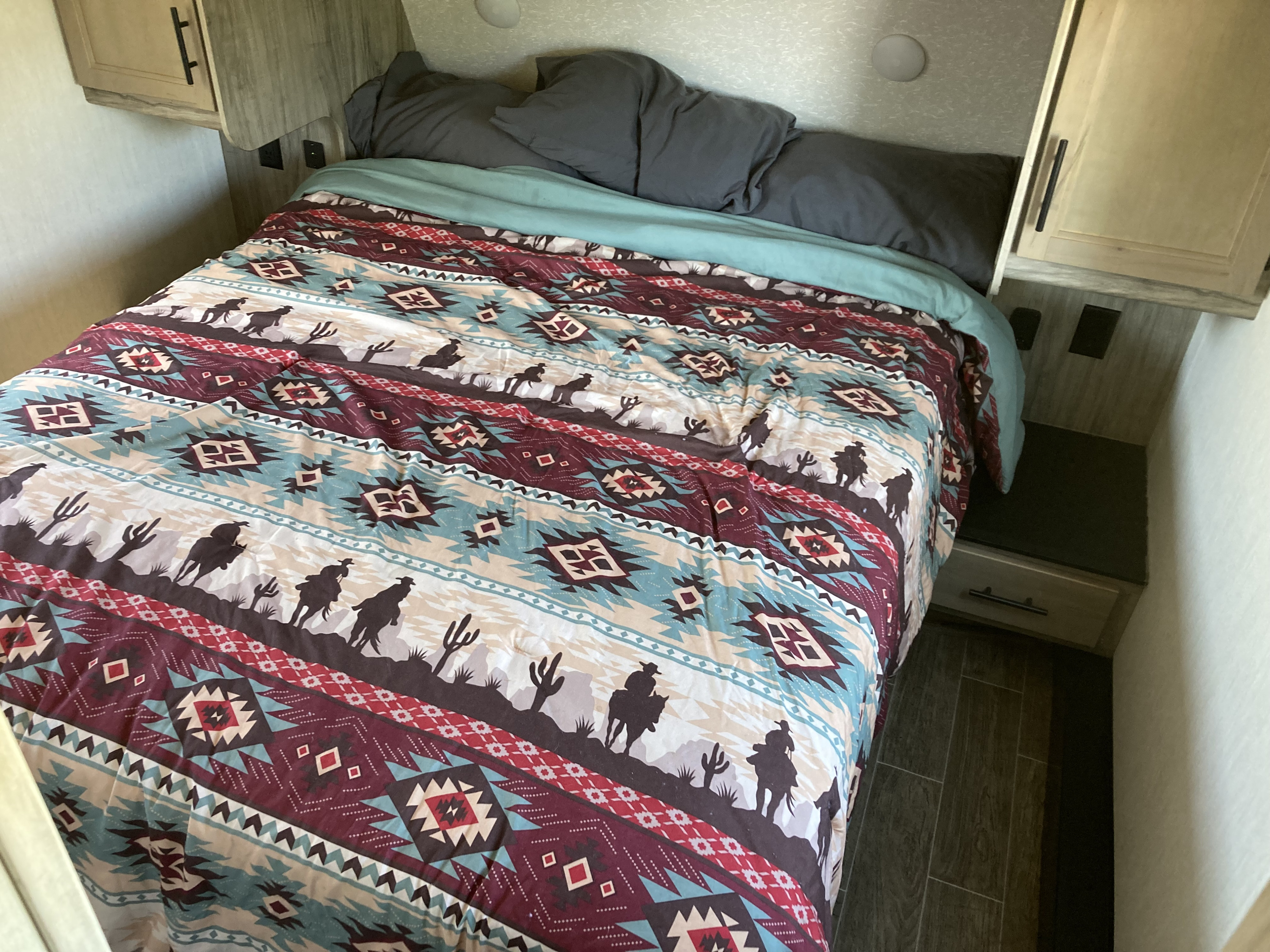 RV rental bedroom: Cozy bed with southwestern comforter (cowboys, cacti), wood cabinets, and integrated lighting.. Forest River Cherokee Arctic Wolf 2022