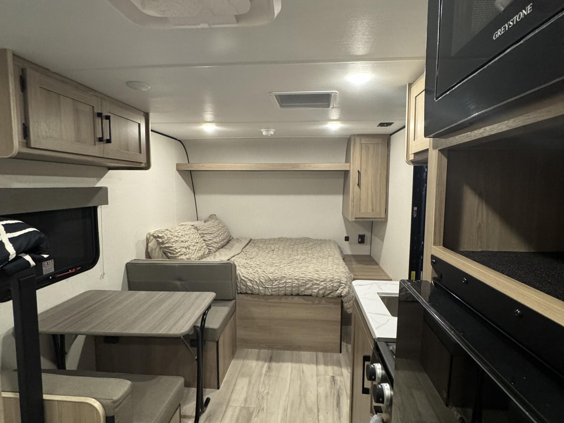 Explore this compact RV rental interior! Features a cozy bed, dinette, and functional kitchen setup.. Keystone Coleman light 17bx 2025