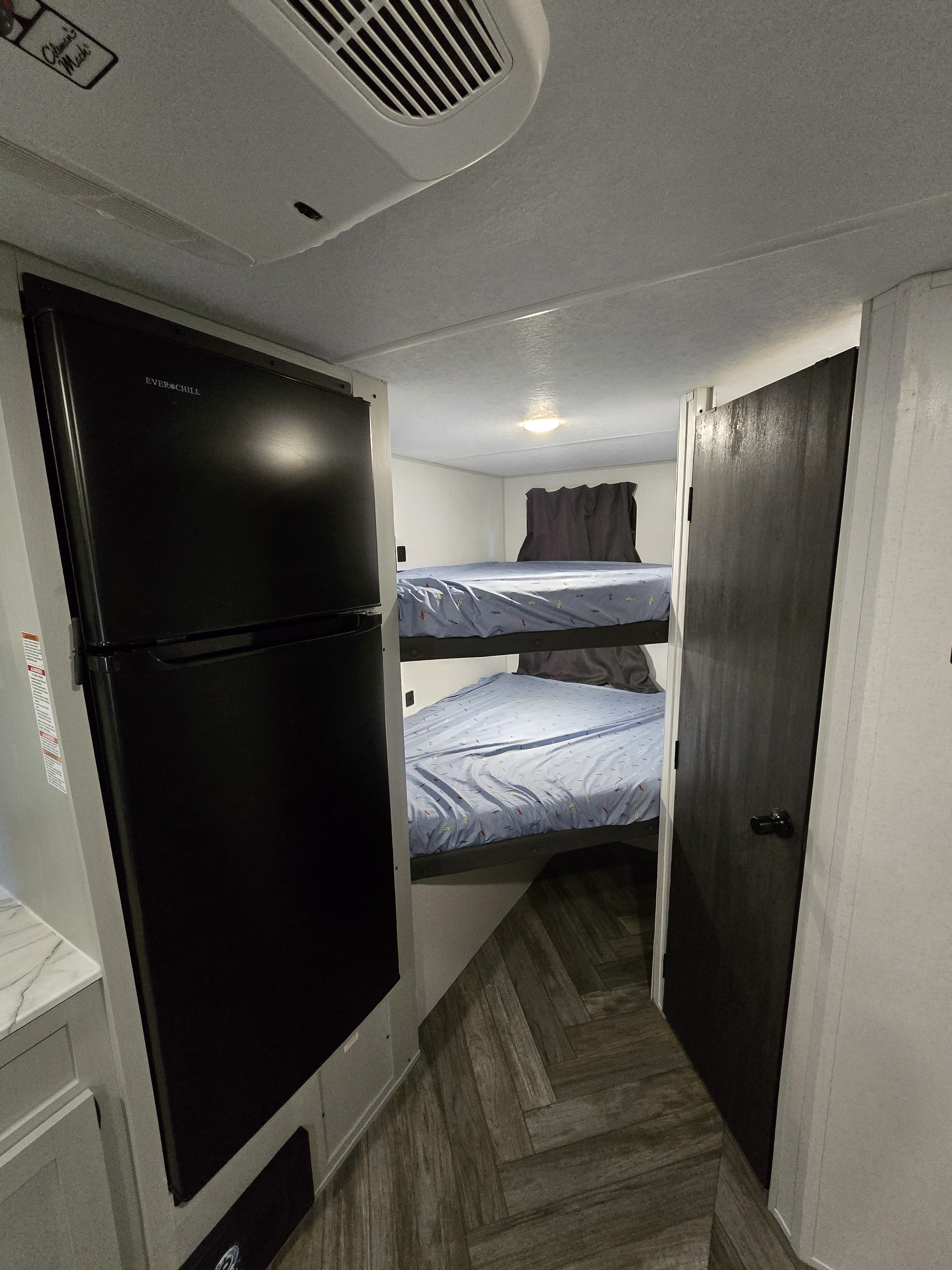 This RV rental interior features a black refrigerator, a hallway leading to cozy bunk beds, and a dark privacy door.. Forest River Salem FSX Plantium 2022