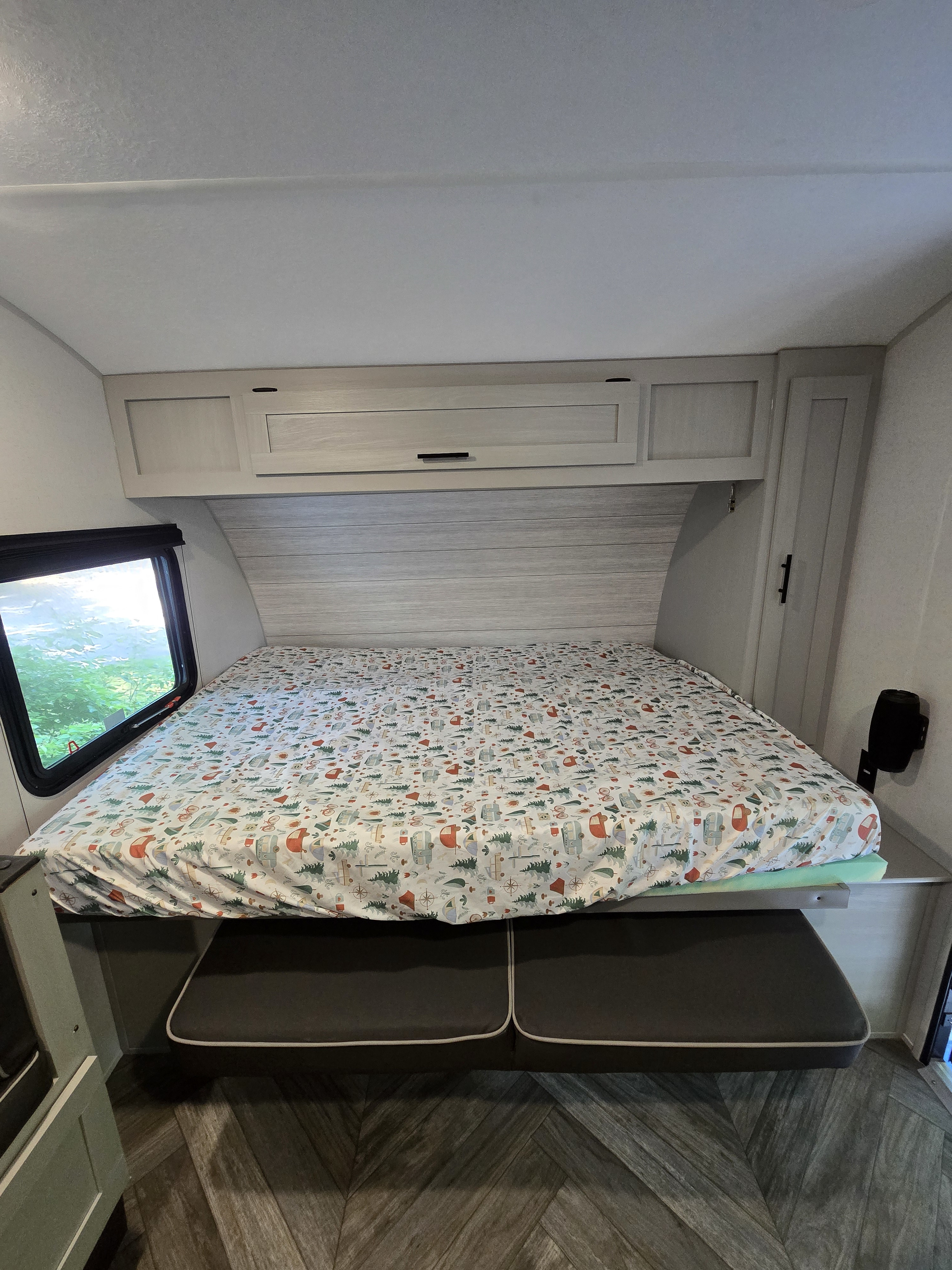 Inside an RV rental: A comfortable bed with a fun camping sheet, overhead storage, and convertible seating below.. Forest River Salem FSX Plantium 2022