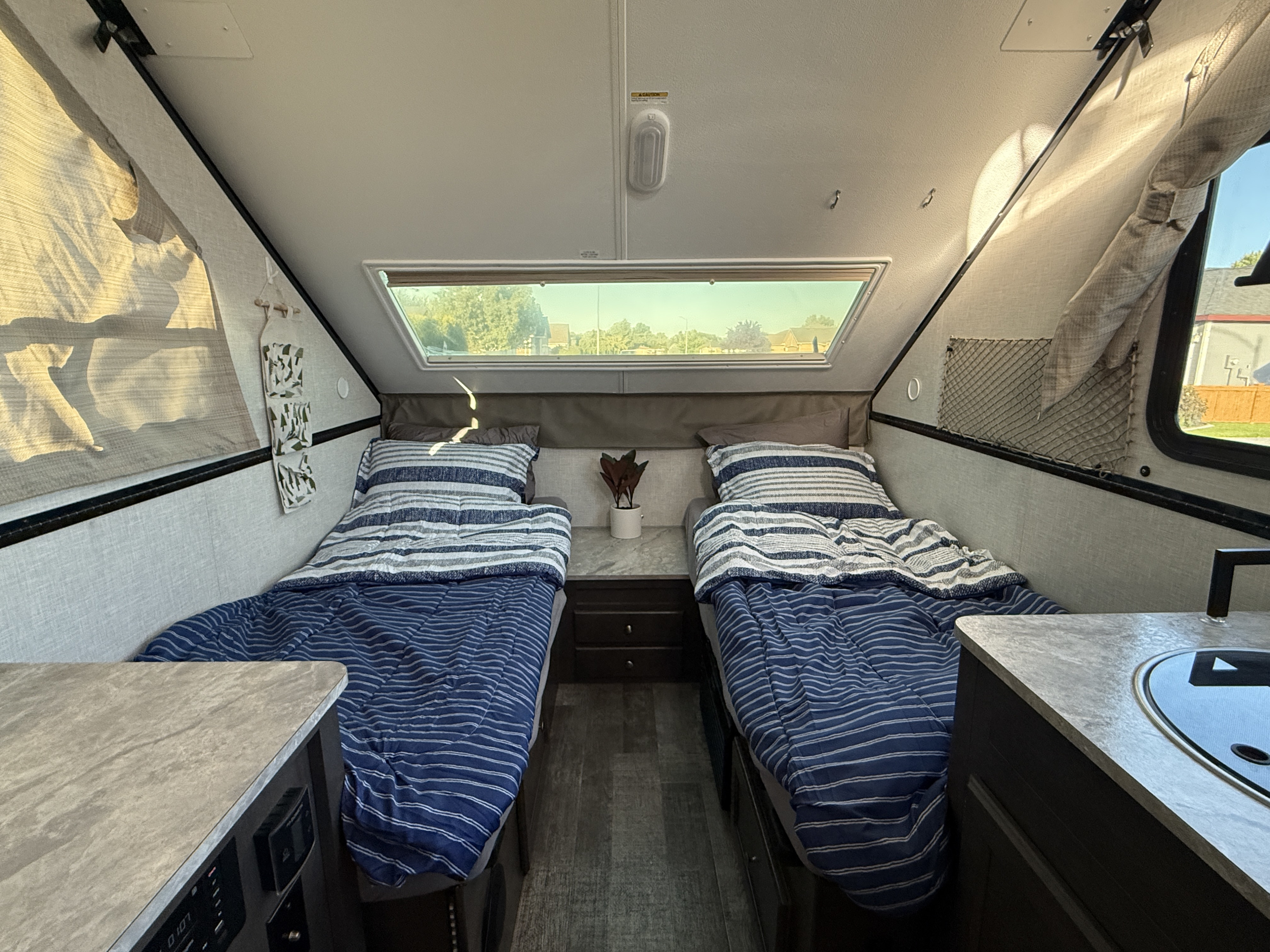 Cozy RV rental interior with two neatly made beds, nightstands, and a large overhead window. Ideal for compact travel.. Forest River Rockwood Premier 2021