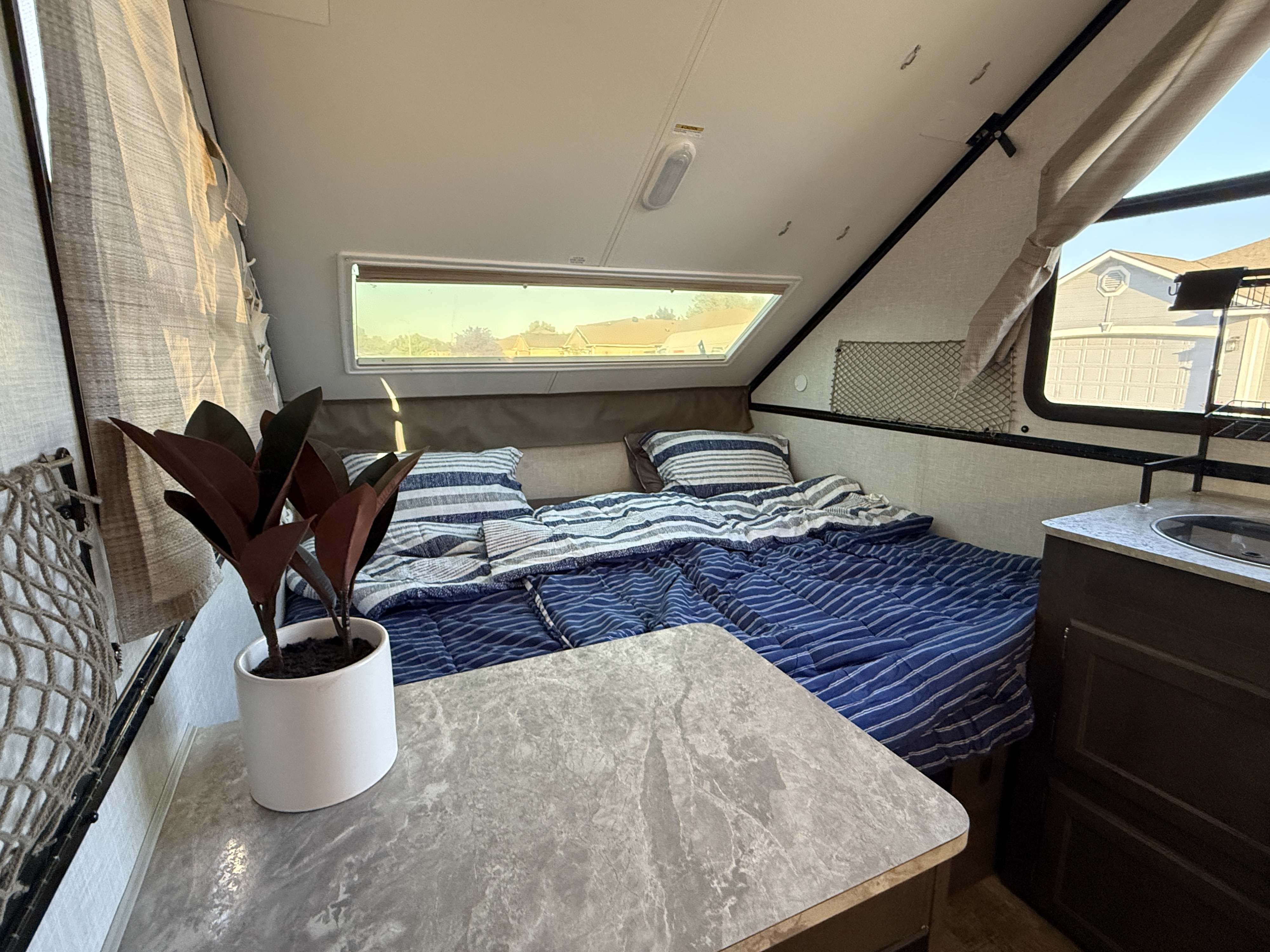 RV rental: Bright interior with a cozy bed, window view of houses, and a compact counter featuring a sink and a plant.. Forest River Rockwood Premier 2021