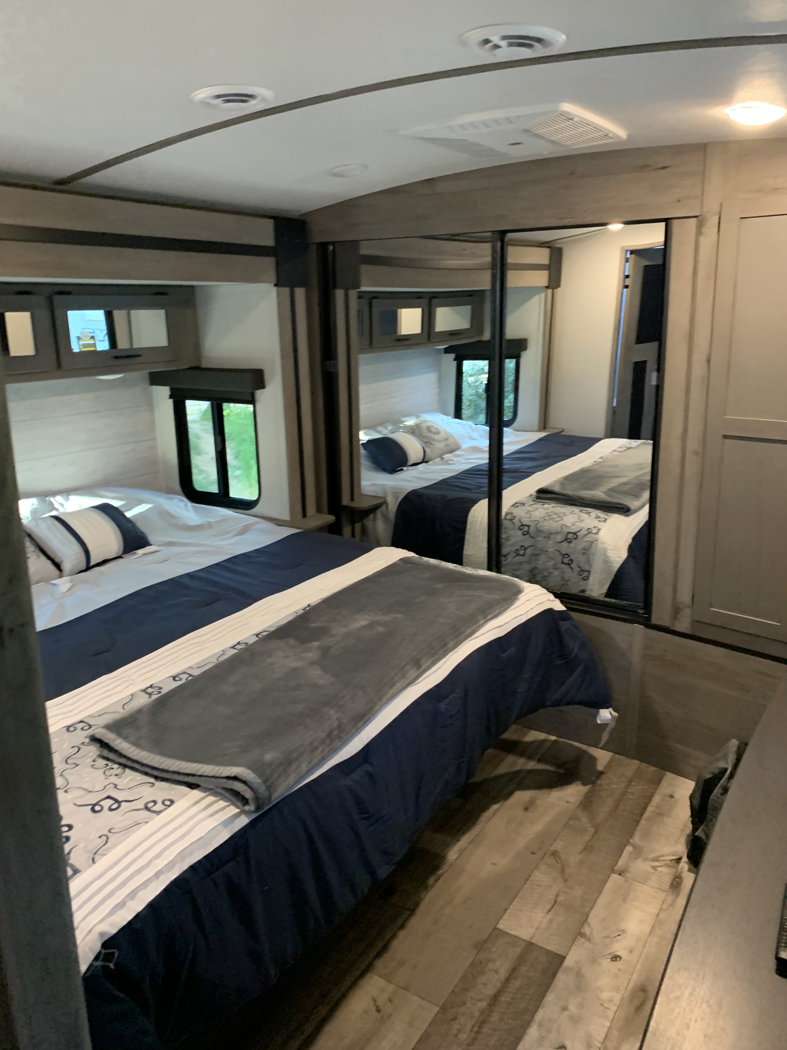 Inside a modern RV rental bedroom featuring a comfortable bed, windows offering views, and mirrored storage.. Keystone RV Hideout 2021