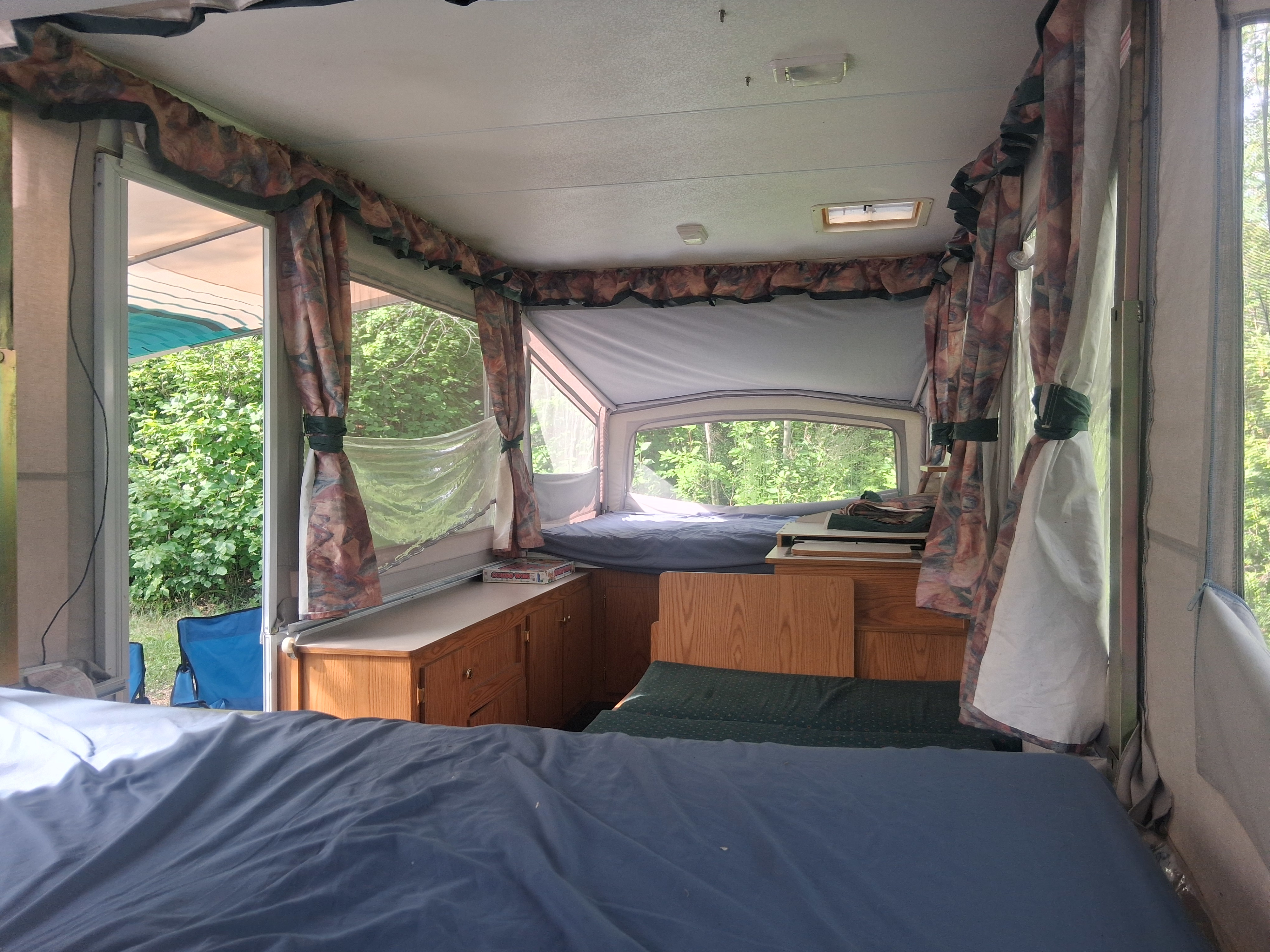 Spacious pop-up camper interior, ideal for an RV rental getaway. Features two beds, cabinets, and panoramic nature views.. Bonair 1050C 1996