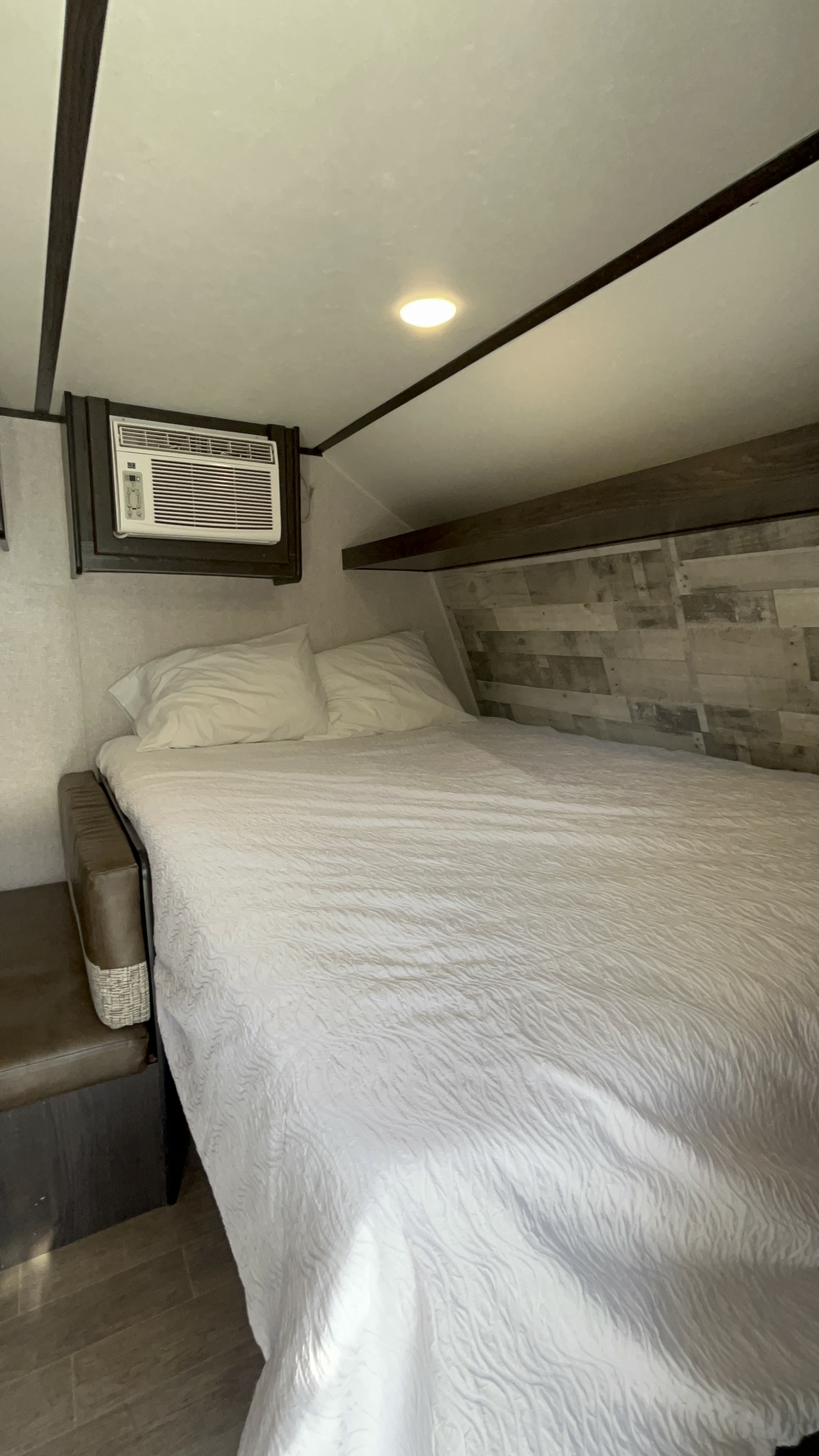 Comfortable RV rental bedroom with a neatly made white bed, pillows, and a wall-mounted AC unit.. Dutchmen Coleman 2021
