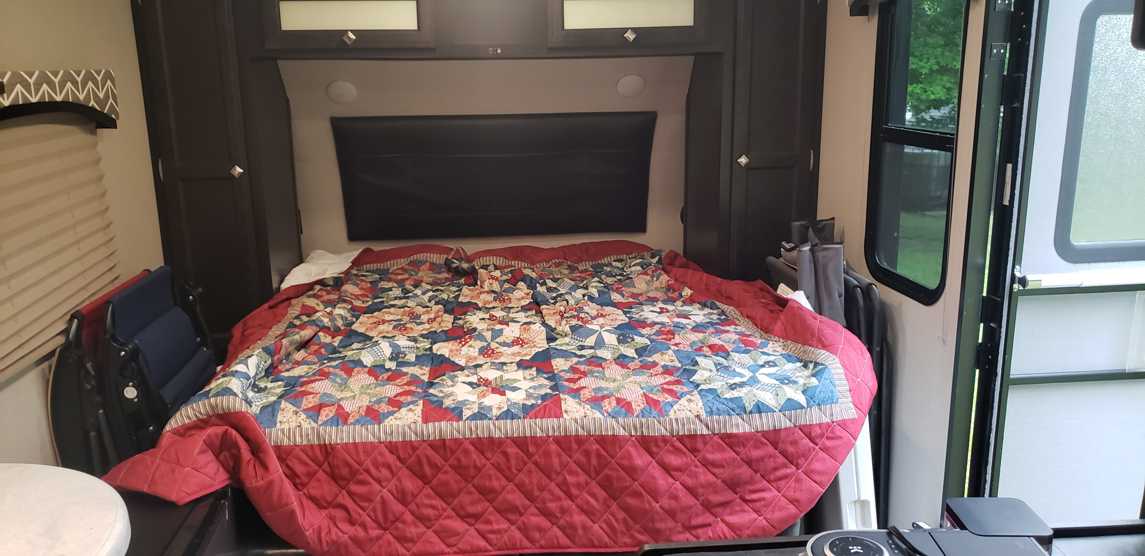 RV rental bedroom: a cozy interior with a vibrant, patterned quilt on the bed, dark cabinets, and a window to nature.. Sonic Sonic Trailer 2018