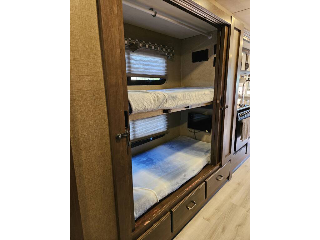 Cozy bunk beds in an RV rental interior, featuring two sleeping spaces, windows with blinds, and a small TV.. Thor Hurricane 2018
