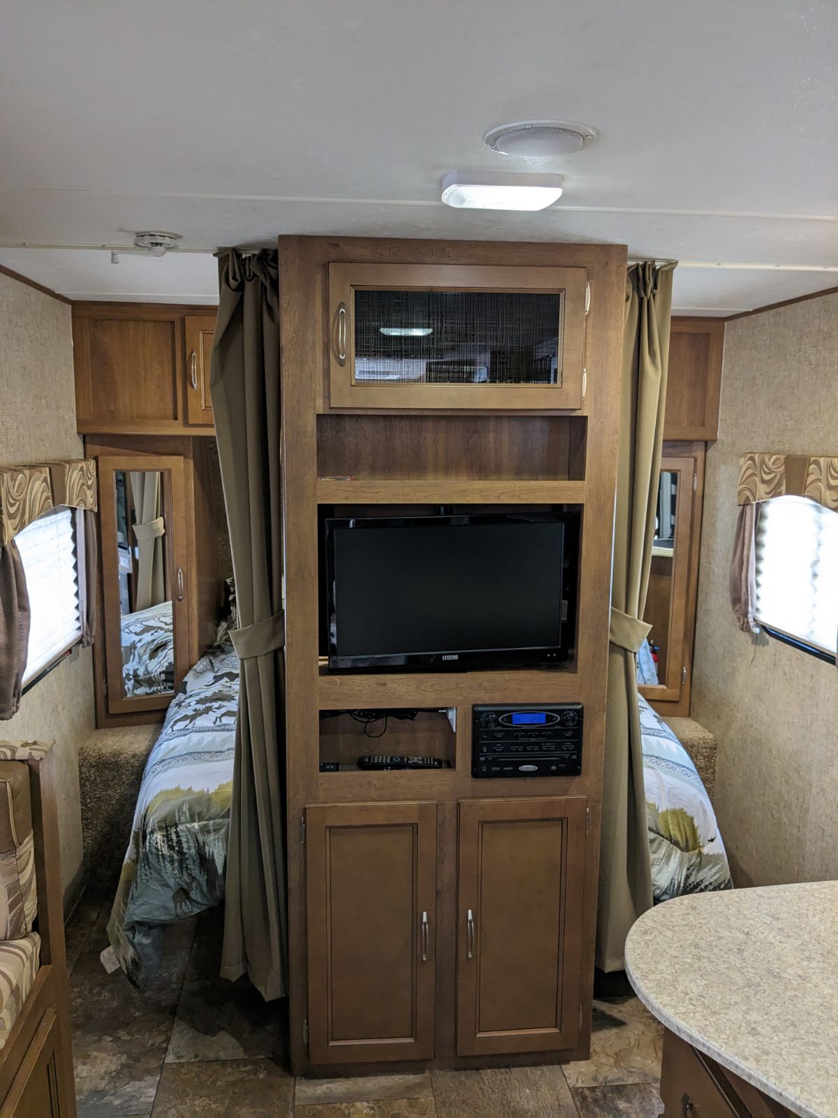 Inside an RV rental: compact bedroom with nature bedding, central entertainment system (TV, stereo), and a kitchen counter.. Coachmen Apex 2014