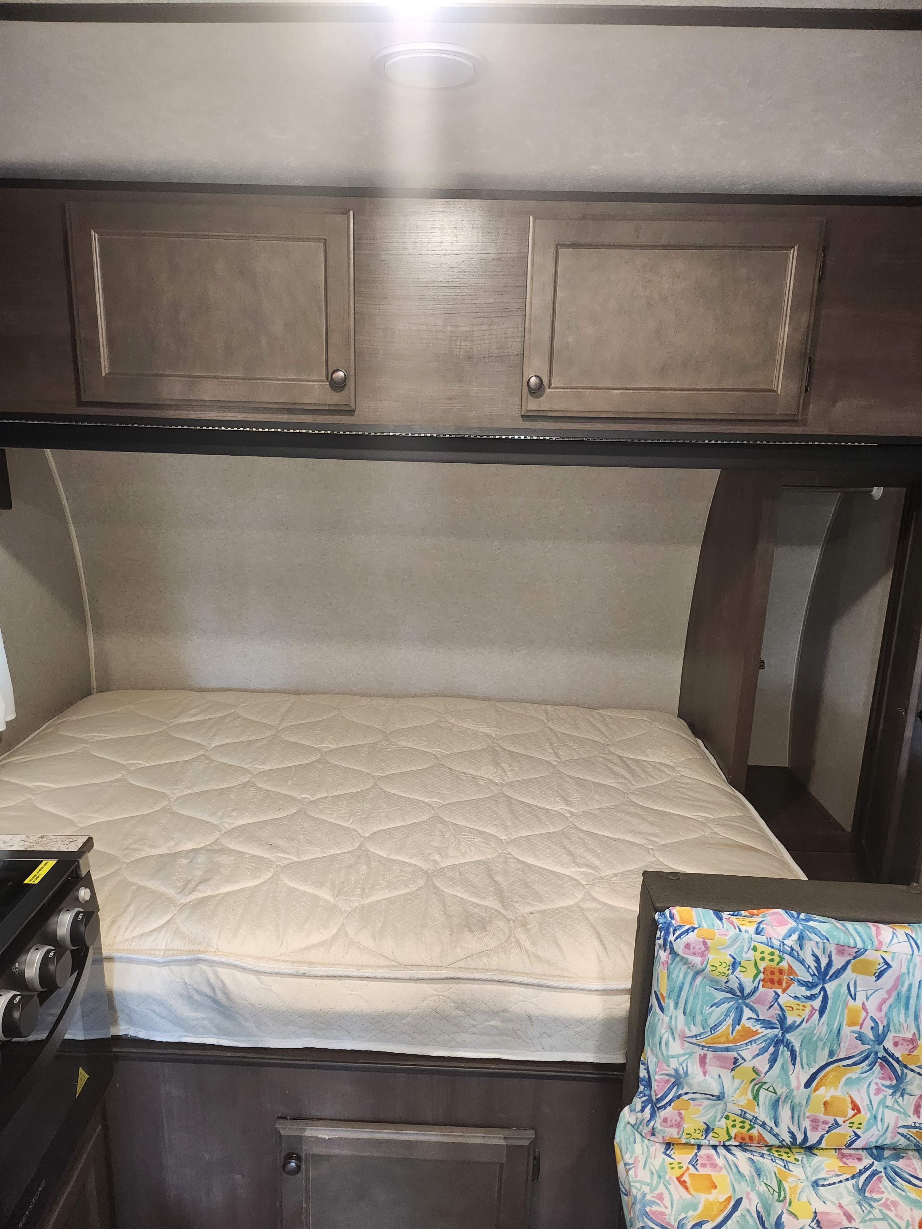RV rental bedroom features: a comfy quilted mattress, wood cabinets, LED lighting, and a colorful tropical pillow.. Sunset Park RV Sun Lite 2022