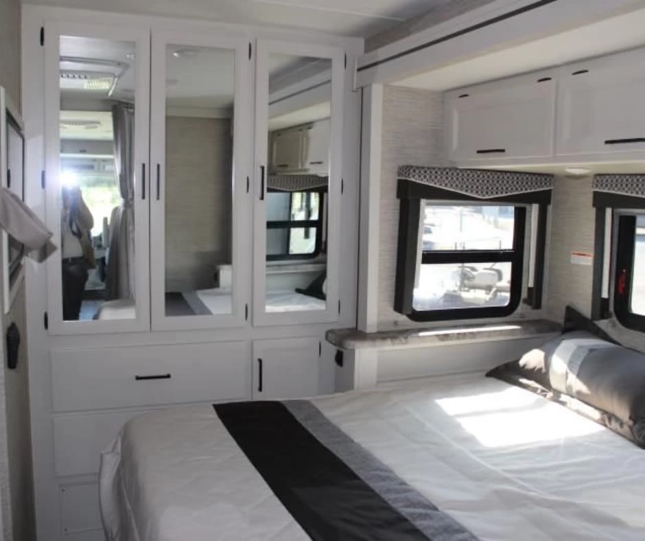 Modern RV rental bedroom interior with clean white cabinets, mirrored storage, and a comfy bed. Bright and spacious.. Thor ACE 29G 2024