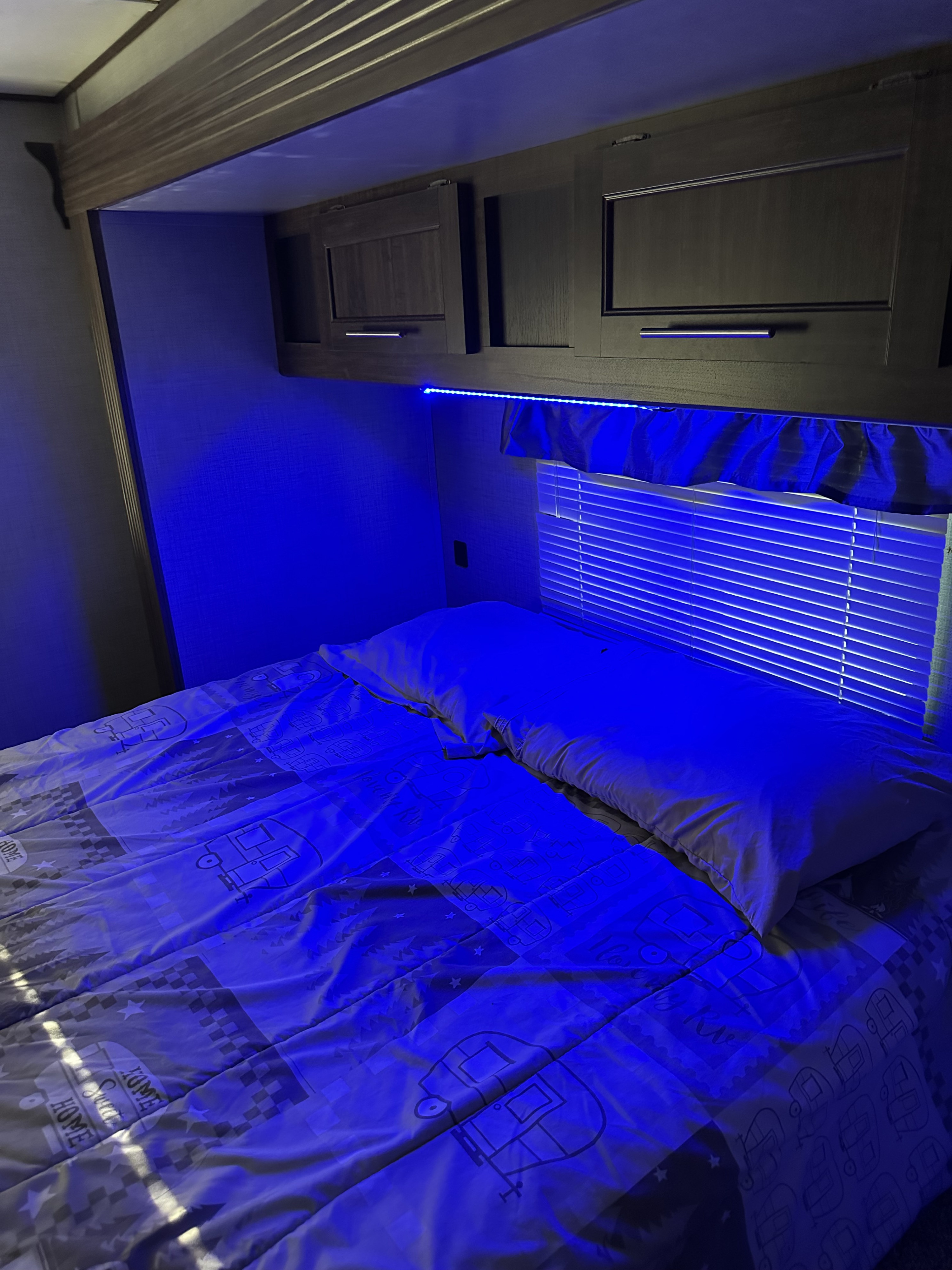Relaxing RV rental bedroom: blue LED lighting illuminates the bed with camper-patterned comforter and overhead storage.. Crossroads RV Zinger 2019
