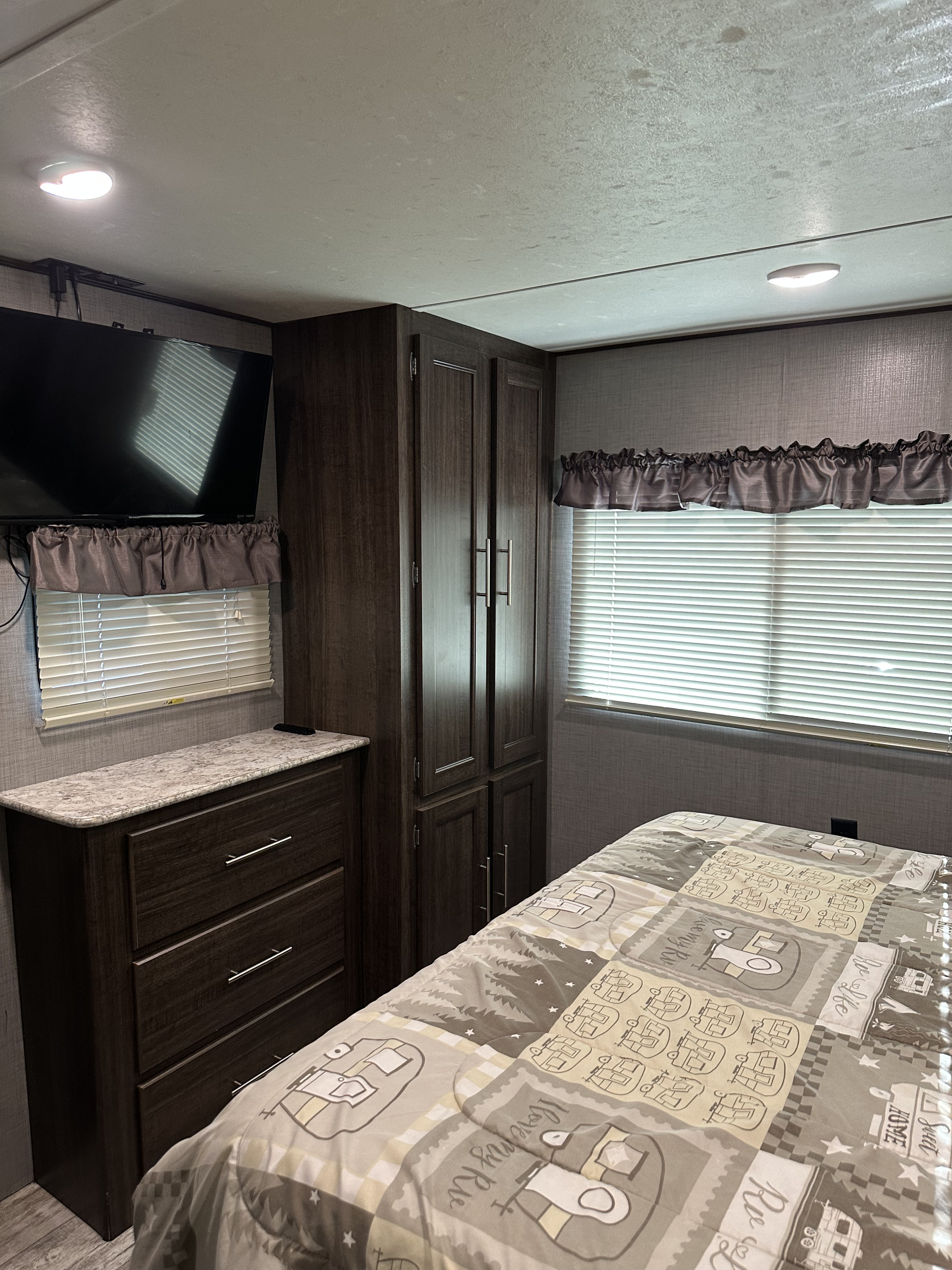 Inside an RV rental bedroom: compact space with dark wood storage, TV, and camping-themed comforter.. Crossroads RV Zinger 2019