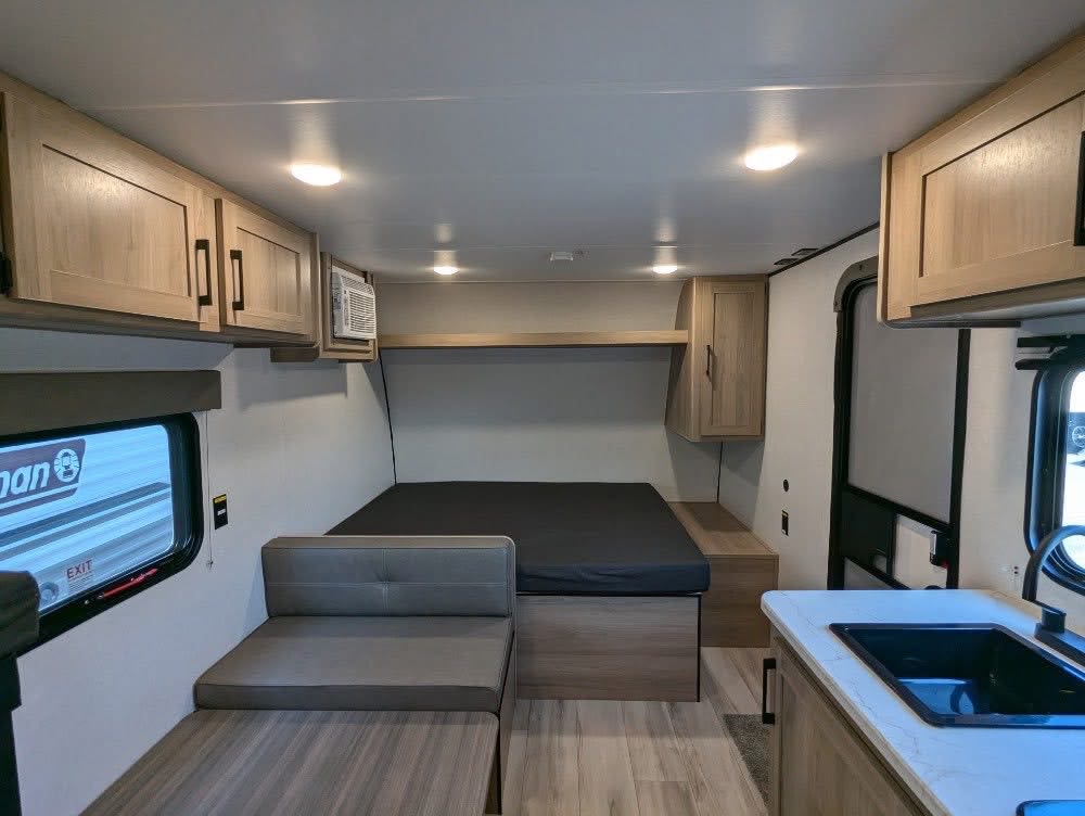 This rv rental interior features a compact living space with a bed, dinette, and kitchen sink, perfect for travel comfort.. Keystone Coleman 2025