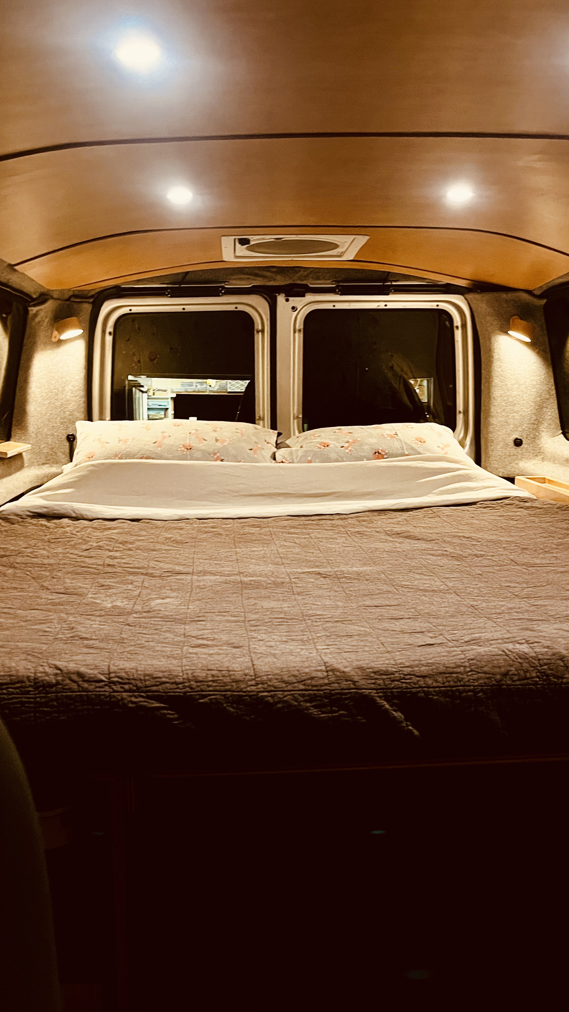 Inside a cozy RV rental: a comfortable bed with soft lighting and rear windows, perfect for serene travel in a camper van.. Ford Econoline 2010