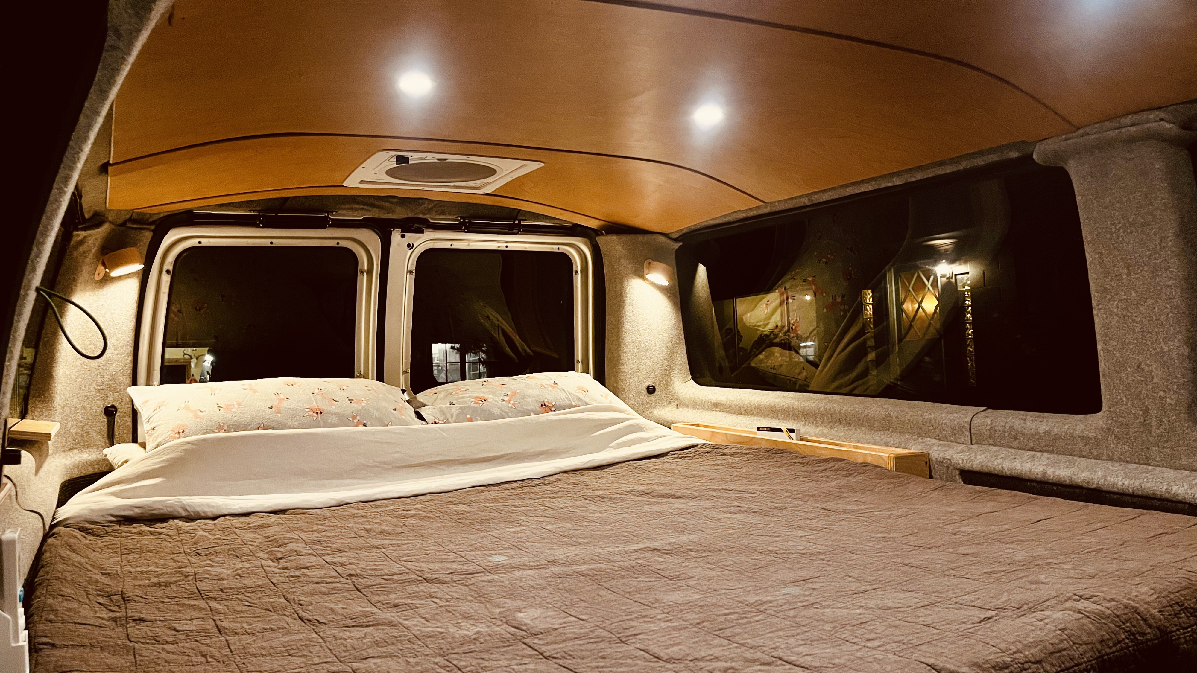 RV rental camper van interior featuring a cozy bed, soft lighting, and wood ceiling at night.. Ford Econoline 2010