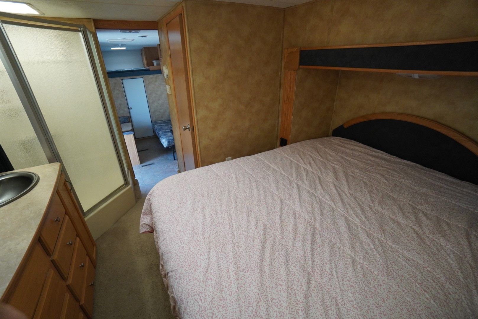 RV rental interior: bedroom with pink patterned comforter, adjacent bathroom with sink and frosted shower, plus a bunk room visible.. Keystone RV Raptor Toy Hauler 2006