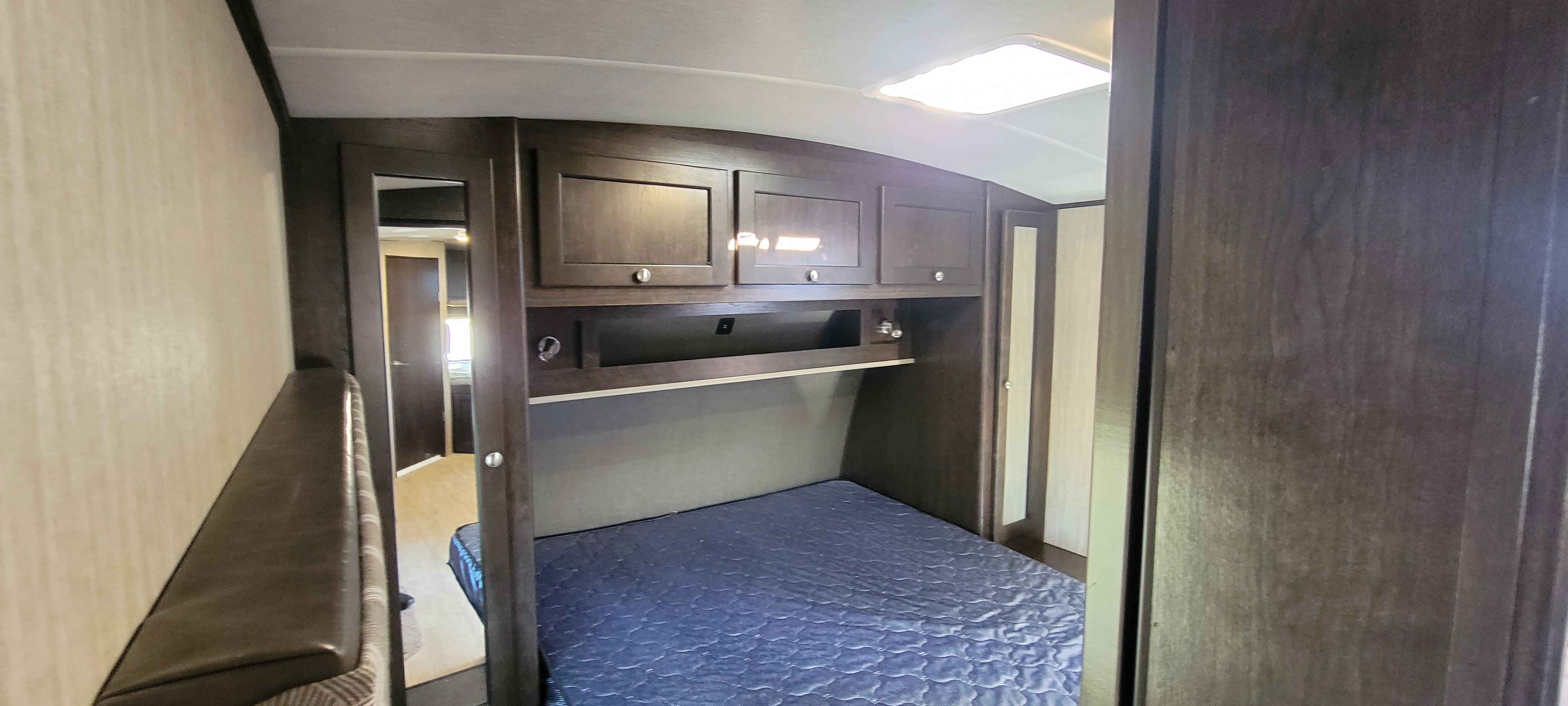 RV rental bedroom with dark wood cabinets above a bed with a blue mattress, offering natural light and storage.. Shadow Cruiser 240RBH 2019