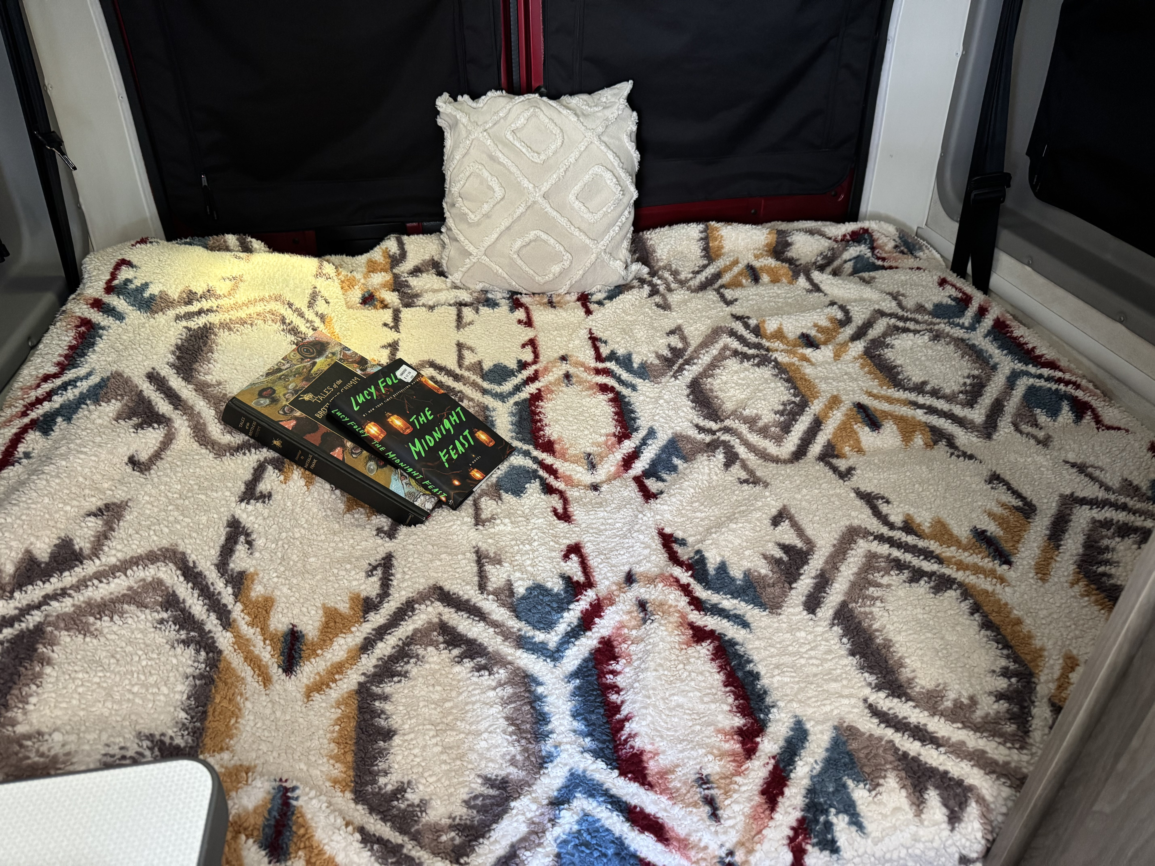 Cozy RV rental bed with patterned sherpa blanket, textured pillow, and books.. Winnebago Solis 2022