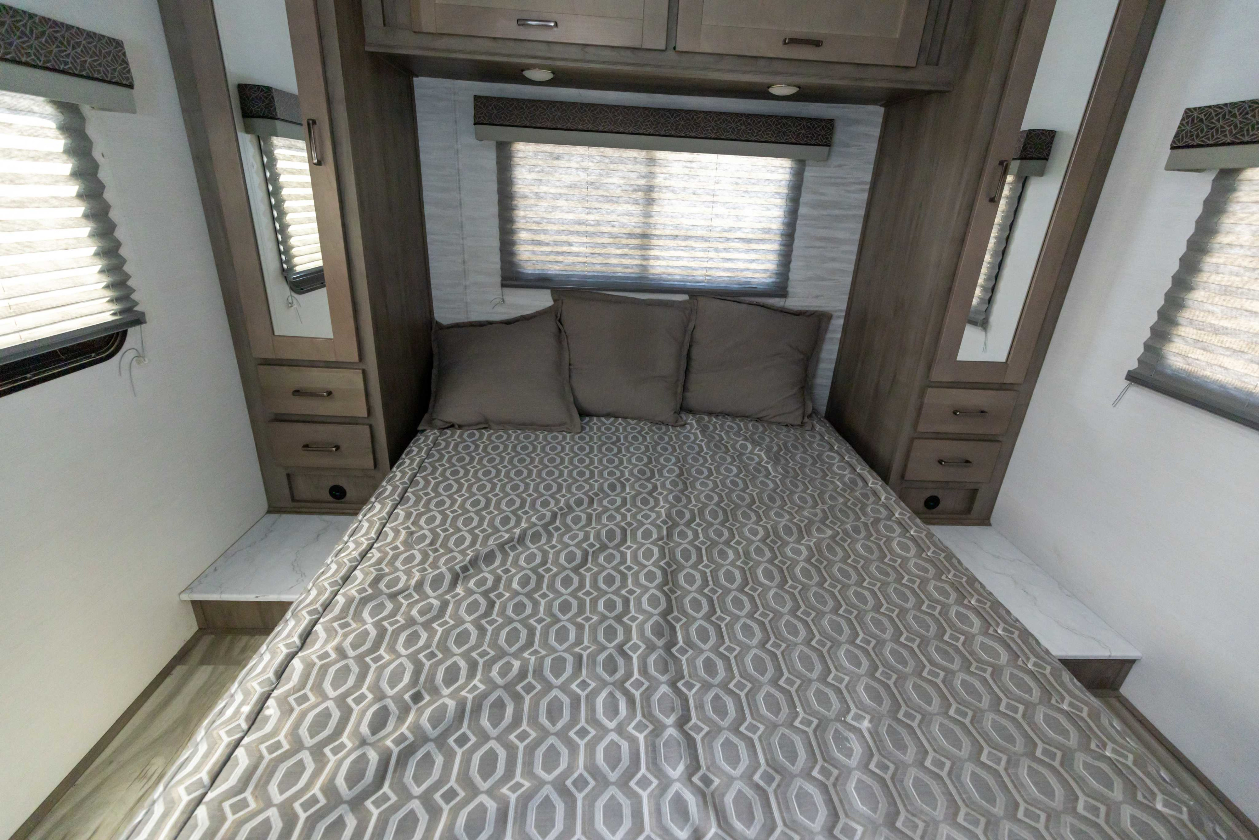 Cozy RV rental bedroom with a comfortable bed, pillows, window blinds, overhead cabinets, and integrated side storage units.. Gulf Stream Conquest 2024