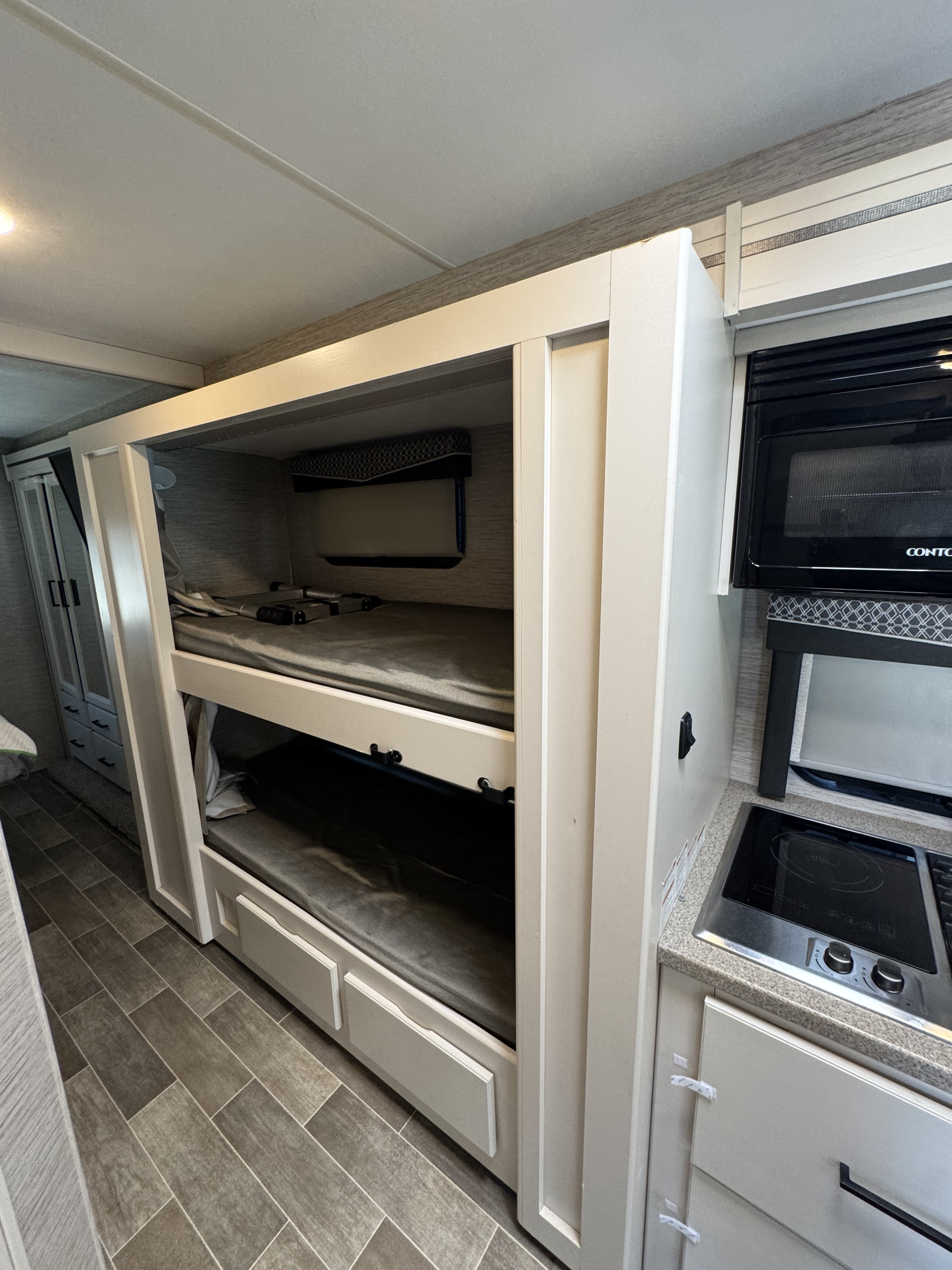 RV rental interior: two-tier bunk beds and a compact kitchen with microwave & cooktop. Bright, functional space.. Four Winds Chateau 2022
