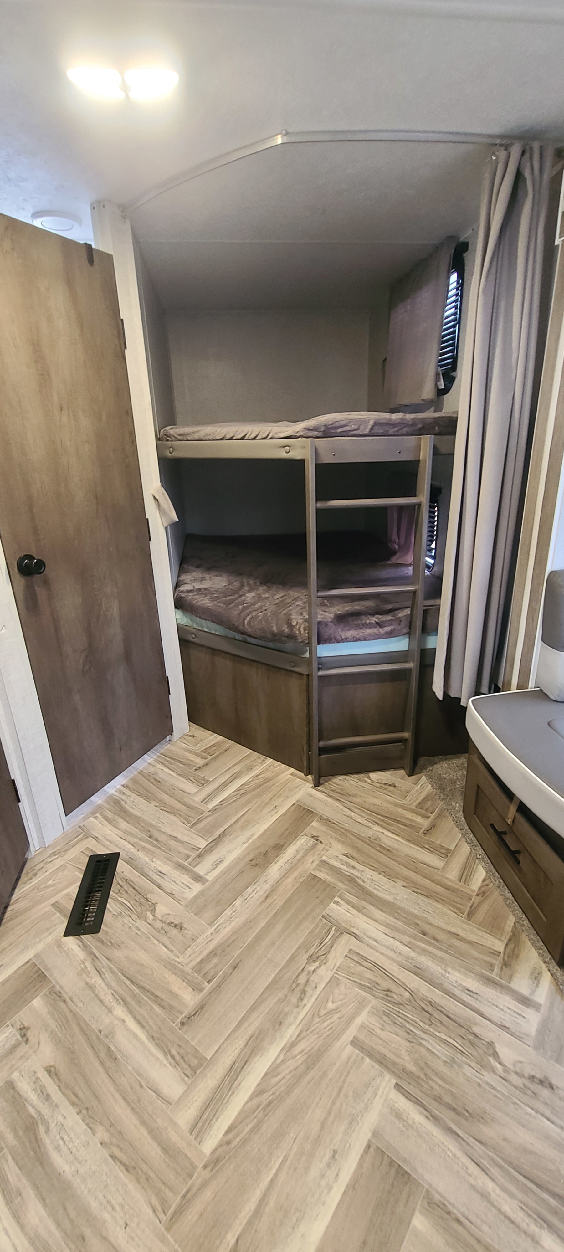 Cozy RV rental interior featuring bunk beds with mattresses & a bright light, plus modern herringbone wood-look flooring.. Forest River Wildwood 2021
