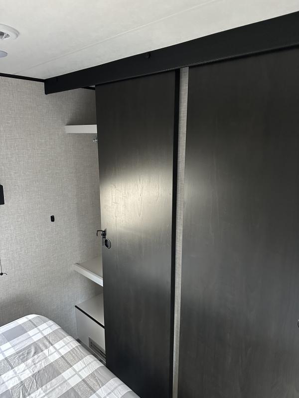 RV rental bedroom: functional storage with dark sliding wardrobe doors and shelves next to a plaid-covered bed.. Jayco Jay Flight 2026