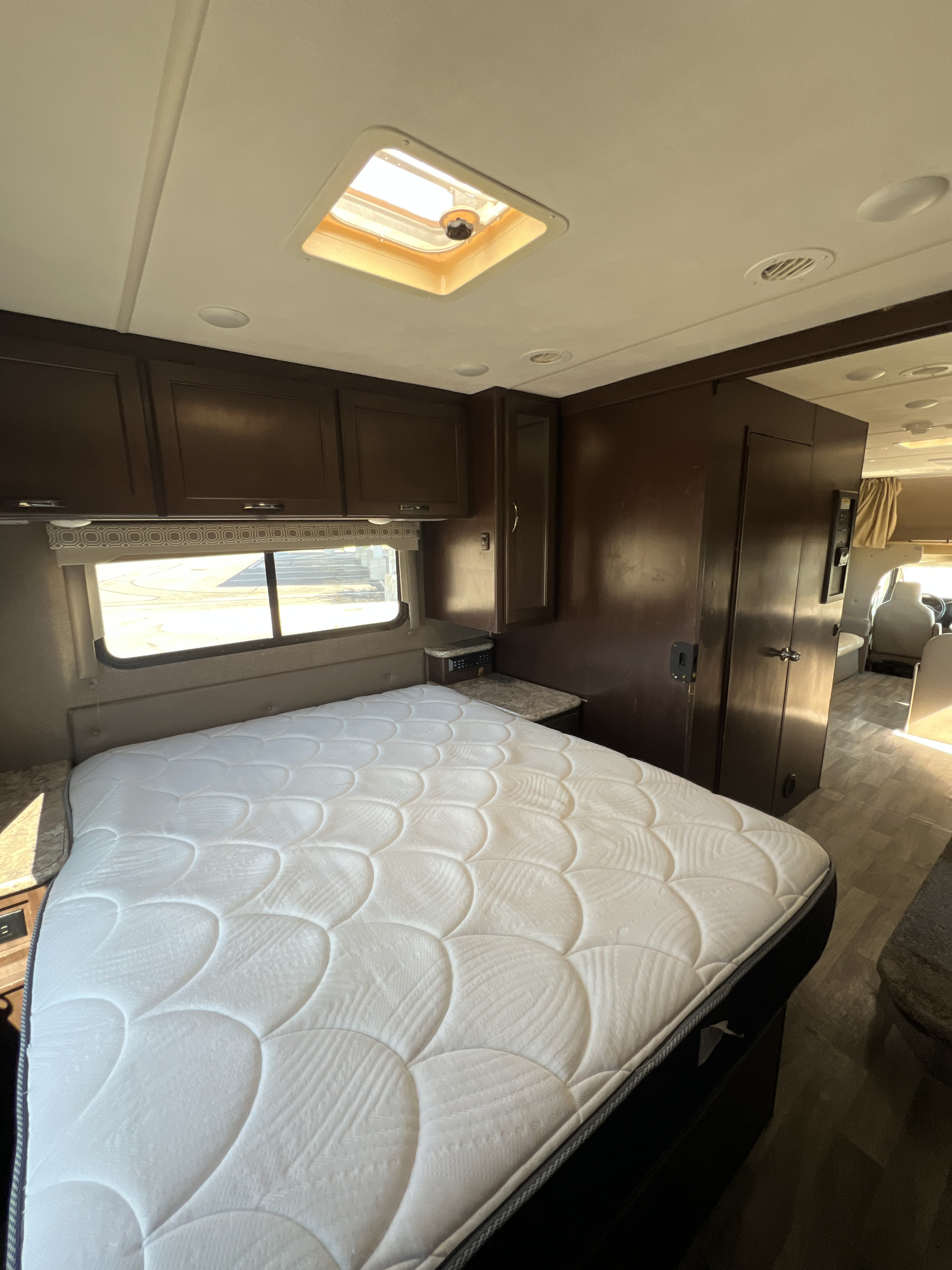RV rental bedroom: a clean white mattress, dark wood cabinets, and a ceiling skylight. Ideal for travel comfort.. Thor Four Winds 2018