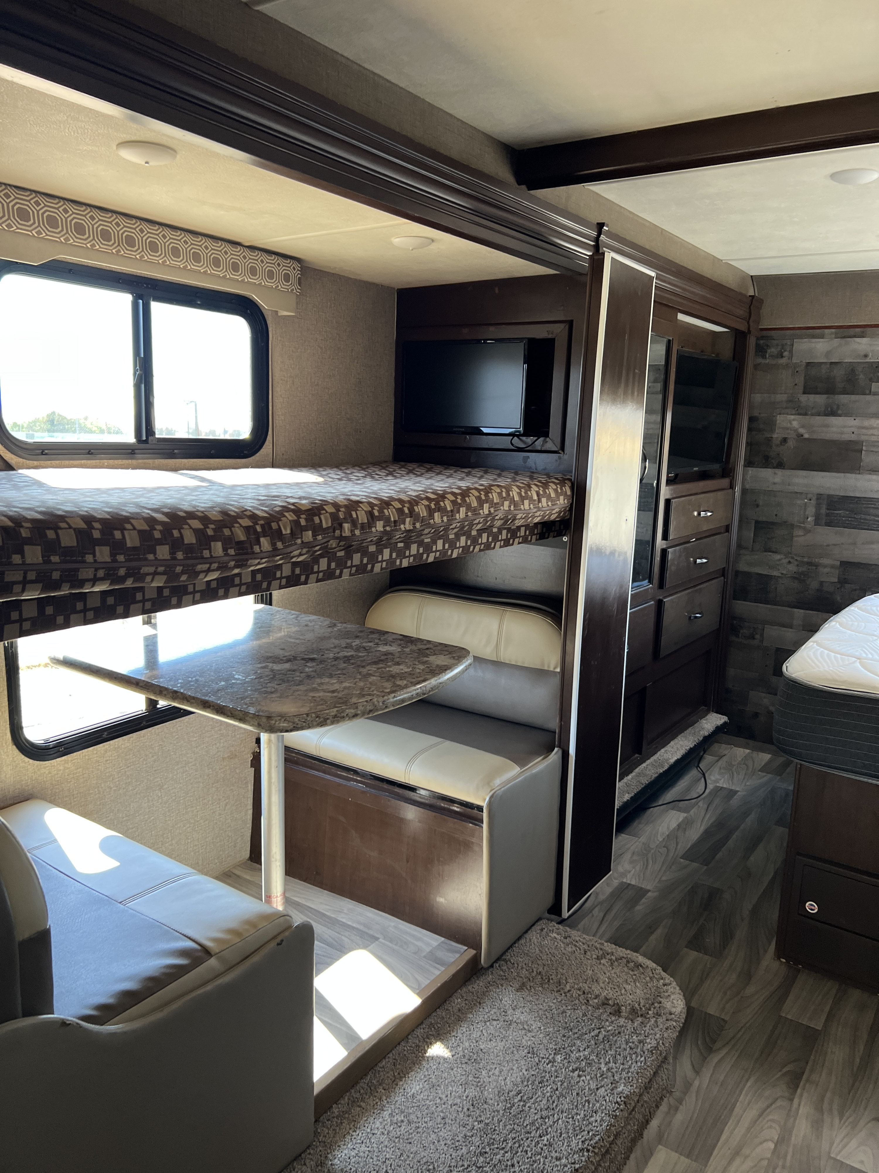 Cozy RV rental interior featuring bunk beds, a dinette with seating, a TV, and a partial view of the main bed area.. Thor Four Winds 2018