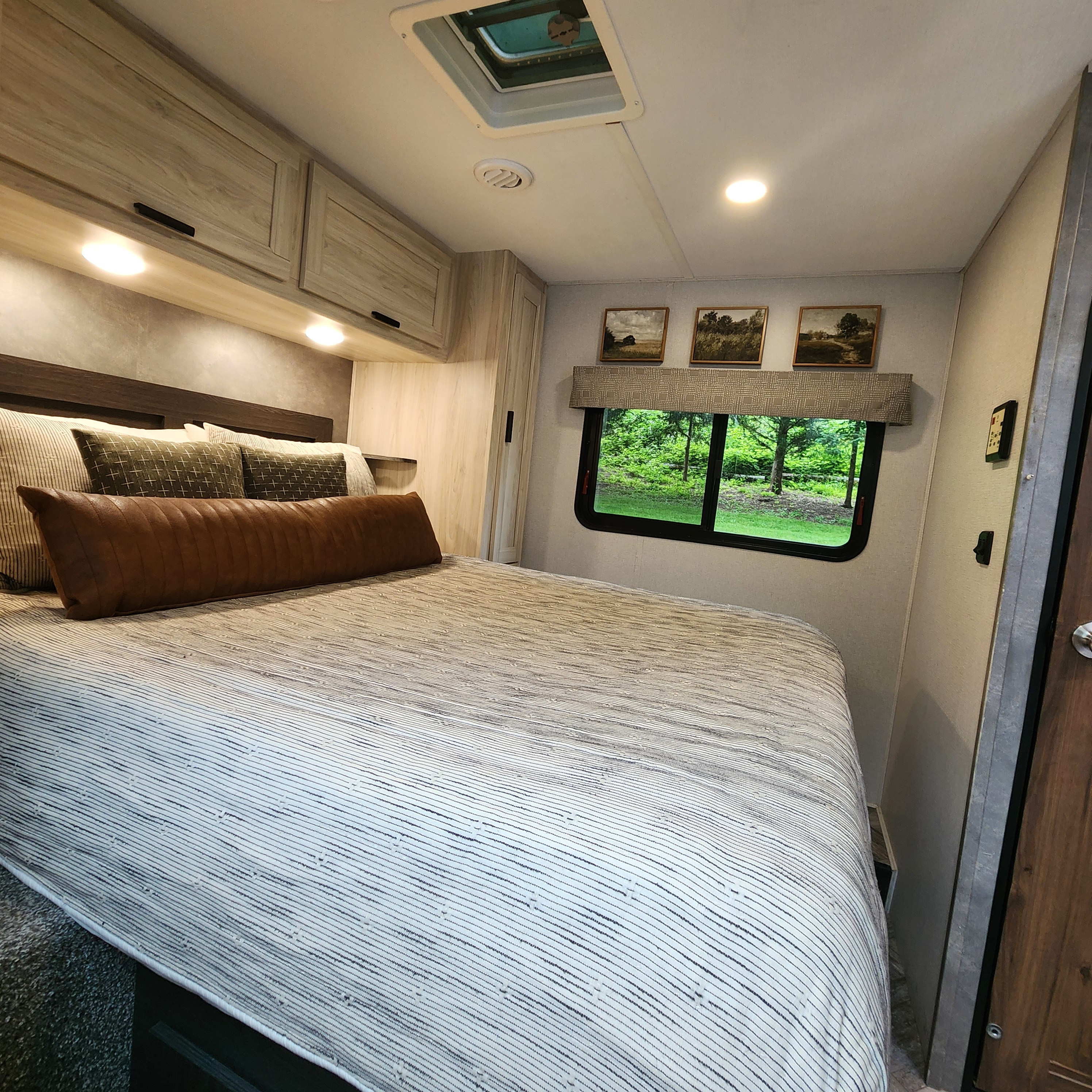 Cozy RV rental bedroom with a comfortable bed, striped bedding, overhead cabinets, and a scenic window view of lush trees.. Forest River Sunseeker LE 2022