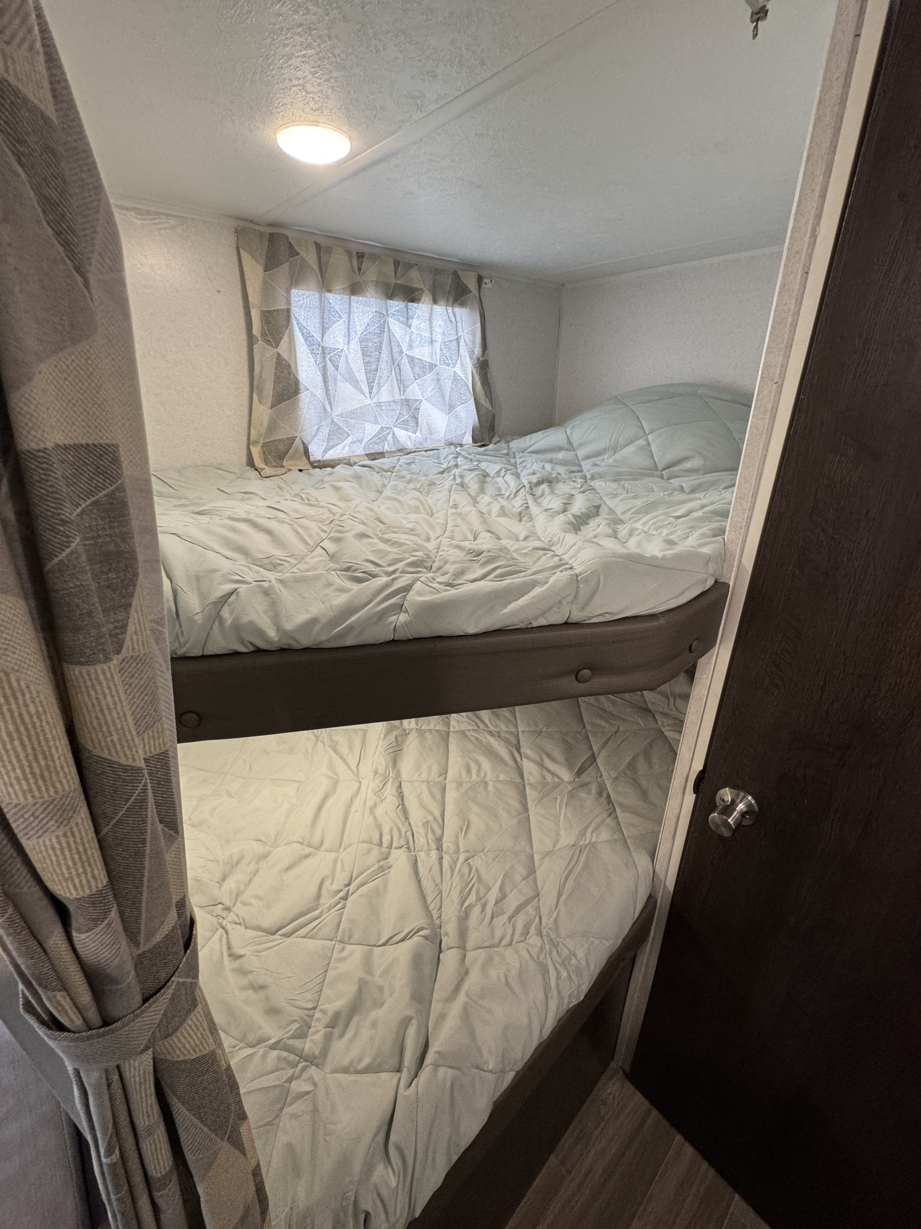 RV rental interior features two bunk beds with comfy light comforters, a window, and a door. Ideal sleeping area.. Forest River Wildwood X-Lite 2019