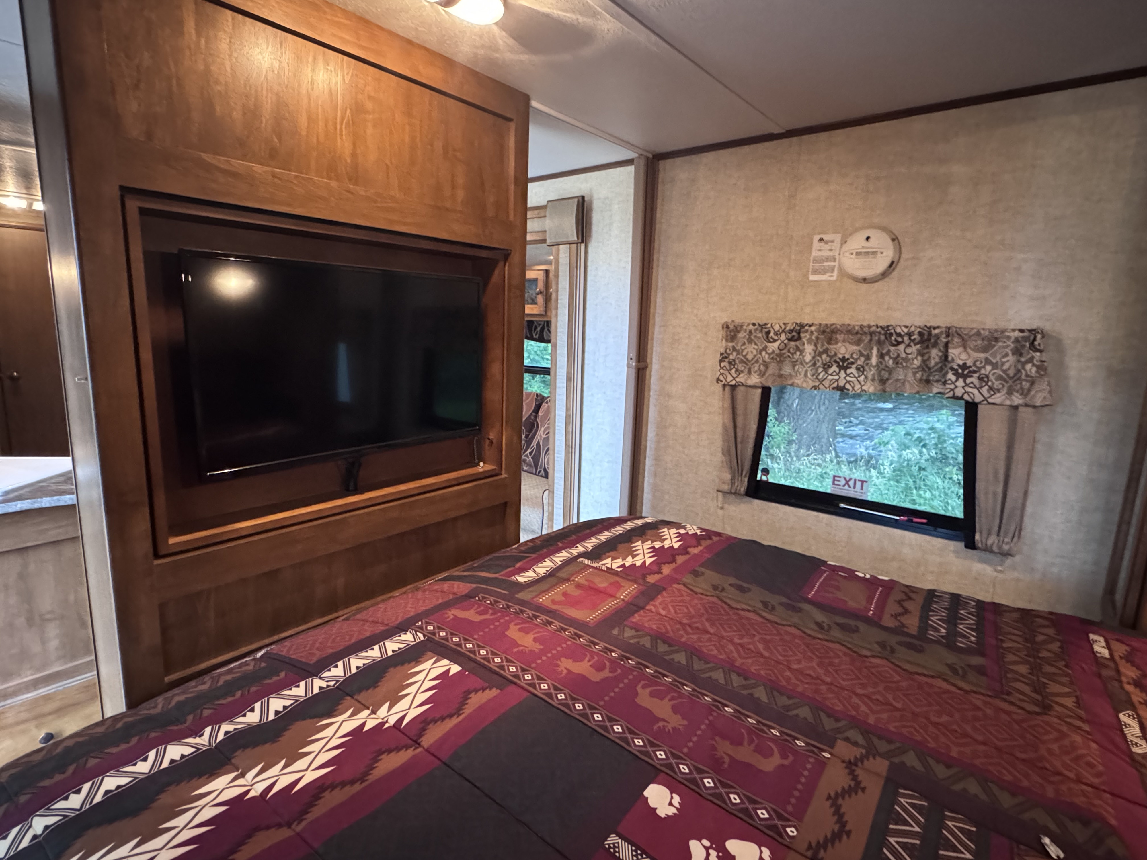 RV rental bedroom interior: a mounted TV, patterned bed, and window revealing lush greenery outside.. Keystone Sprinter 2013