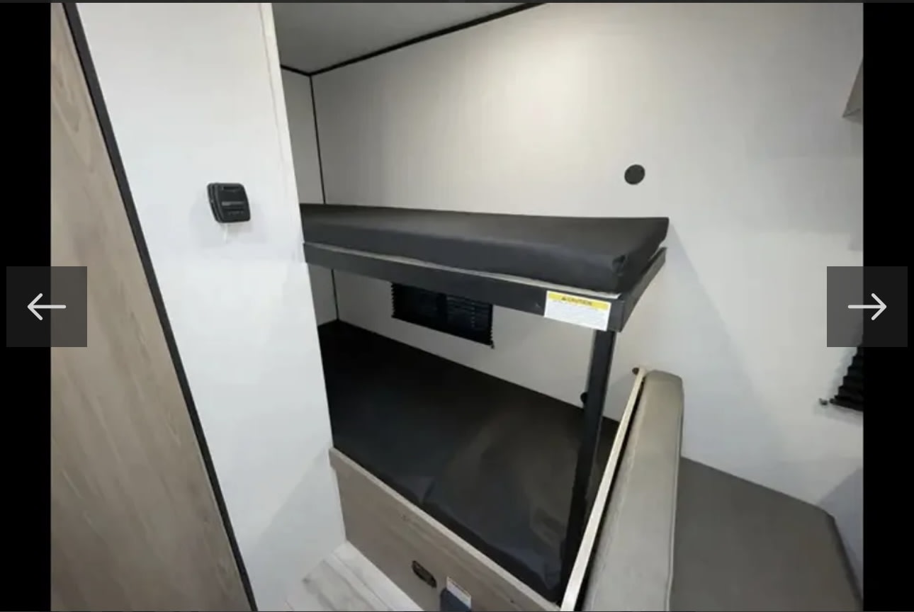RV rental interior: Compact sleeping area with two black bunk beds. A control panel and vent are visible on the white walls.. KEYSTONE COLEMAN 17B 2025