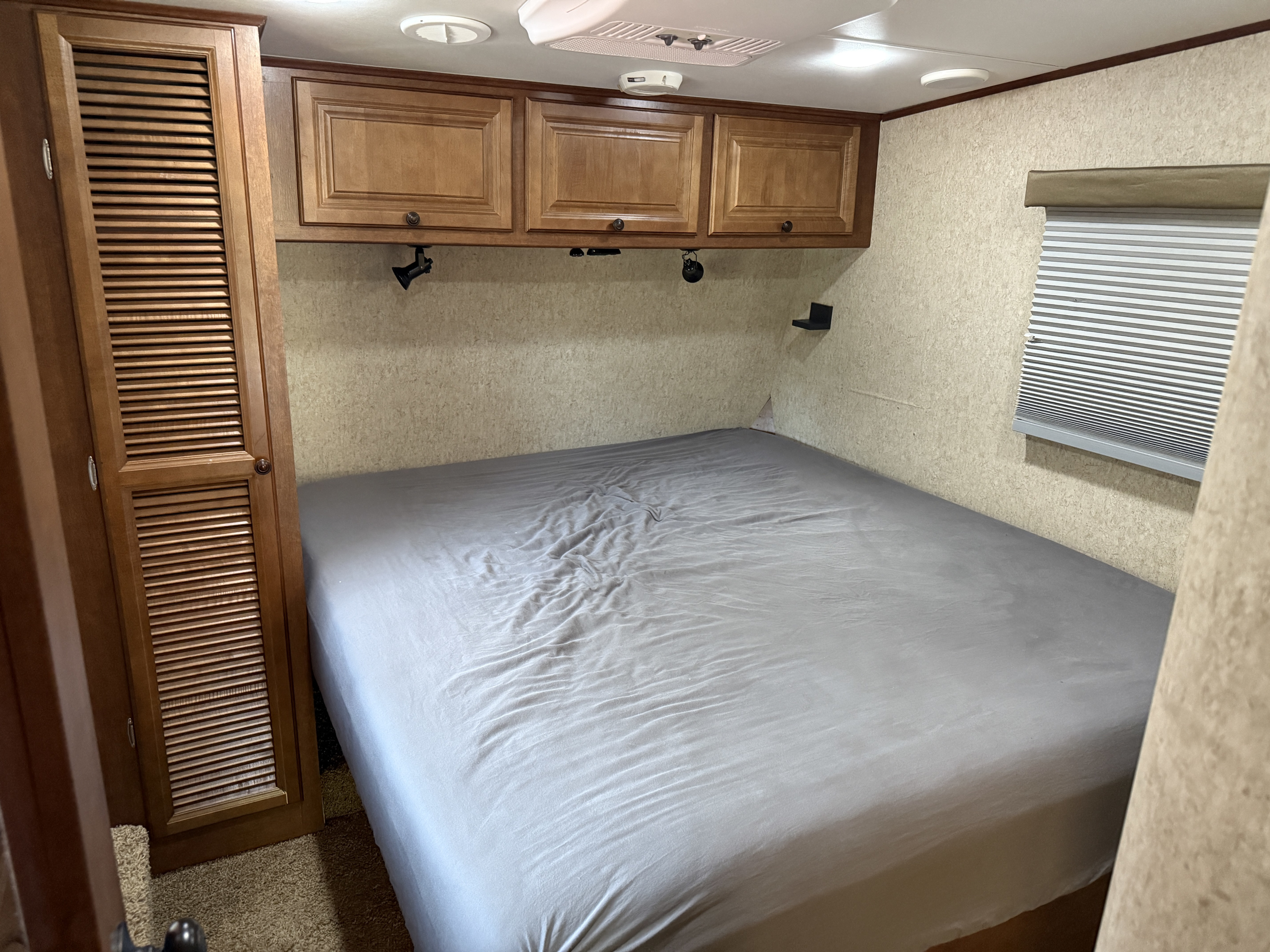 Cozy rv rental bedroom with a queen bed, wooden cabinets & closet, and window blinds, ready for your next adventure.. Heartland RVs Bighorn 2012