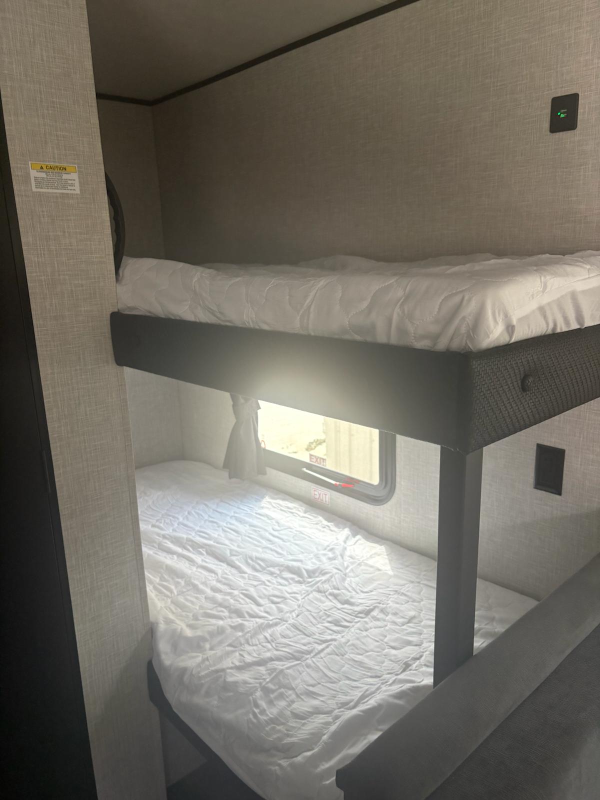 Inside an RV rental: two white-sheeted bunk beds with exit window, offering a comfortable sleeping area.. Jayco Jay Flight SLX 2025