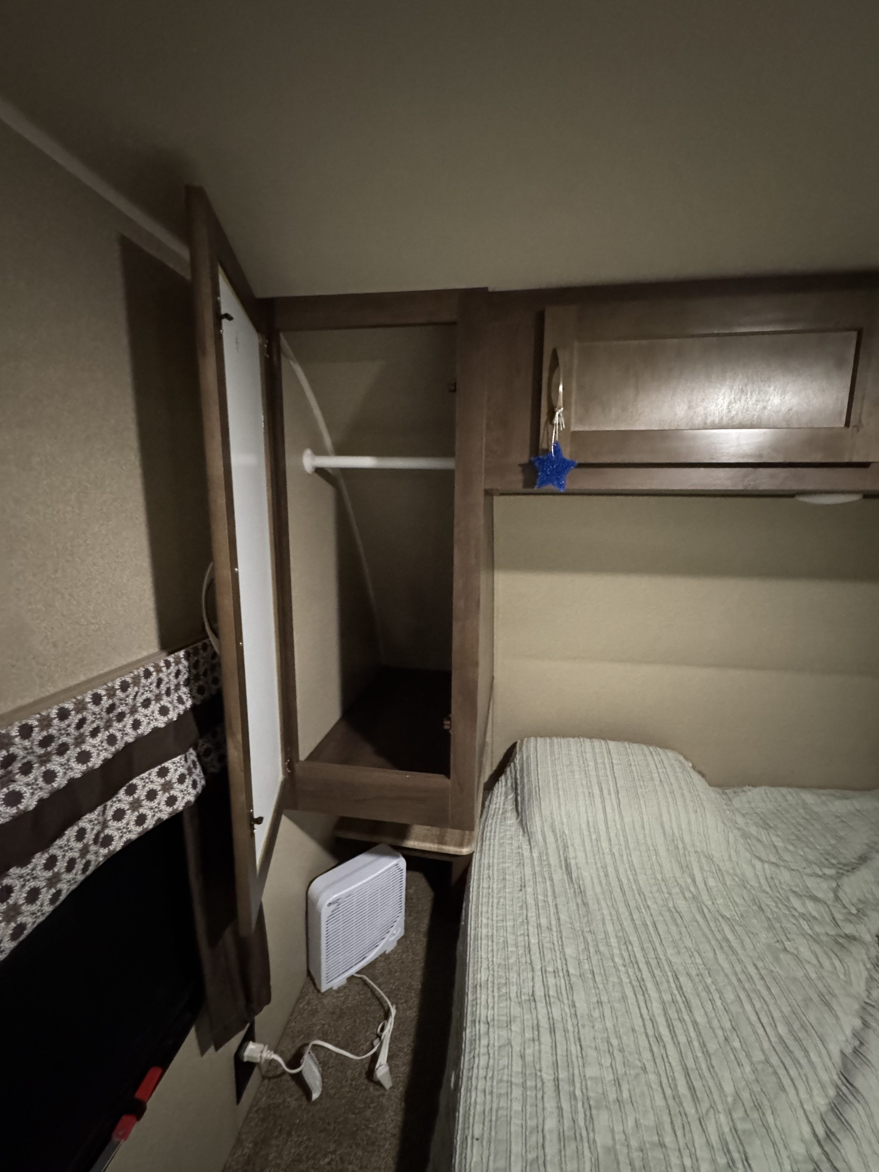 RV rental bedroom with a striped bed, open cabinet (clothes rod visible), and a small fan on the floor.. Forest River Palomino Puma 2018