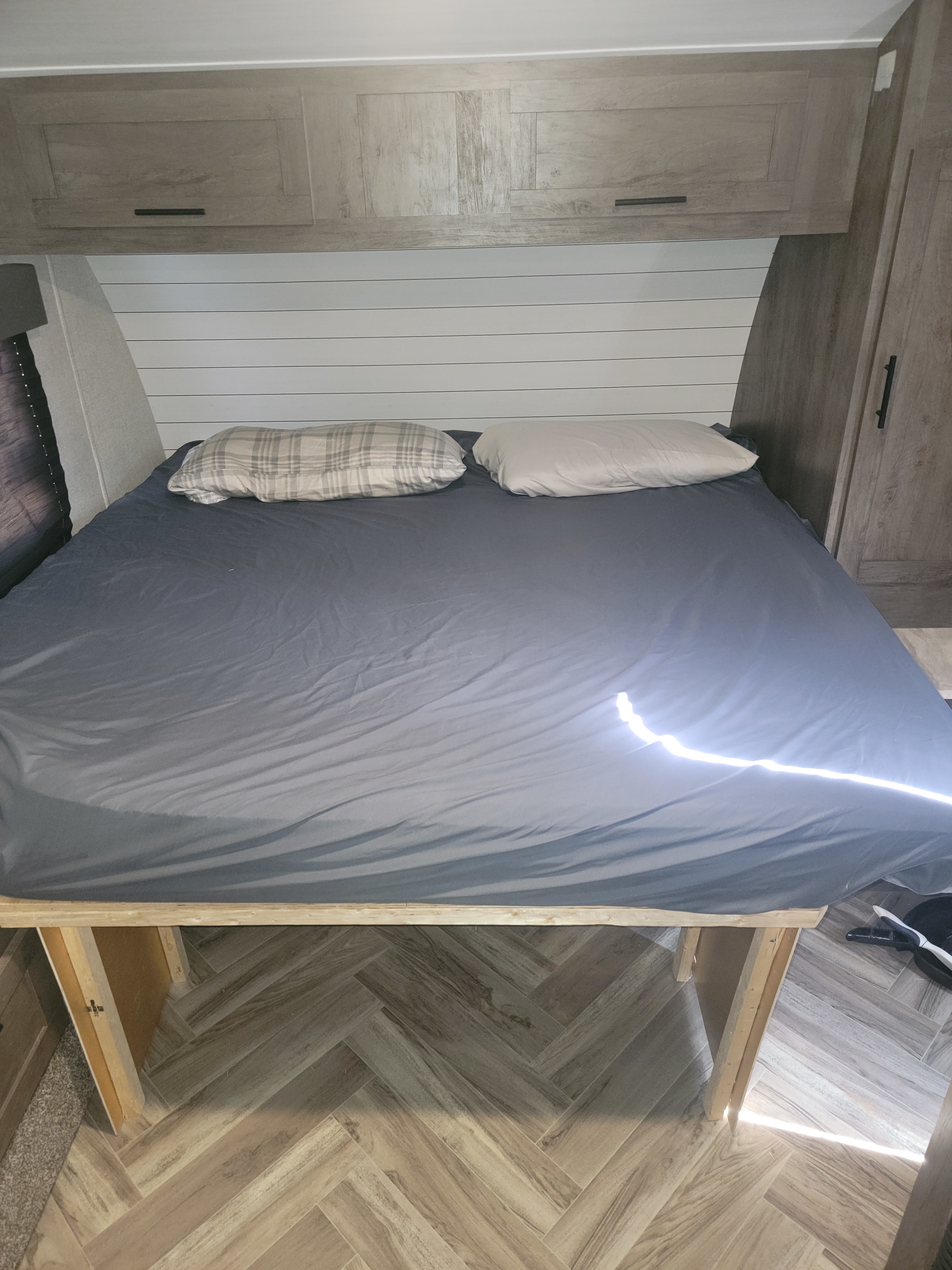 RV rental: A cozy bed with pillows, overhead cabinets, shiplap wall, and wood-look herringbone floor.. Forest River Salem Cruise Lite 2021