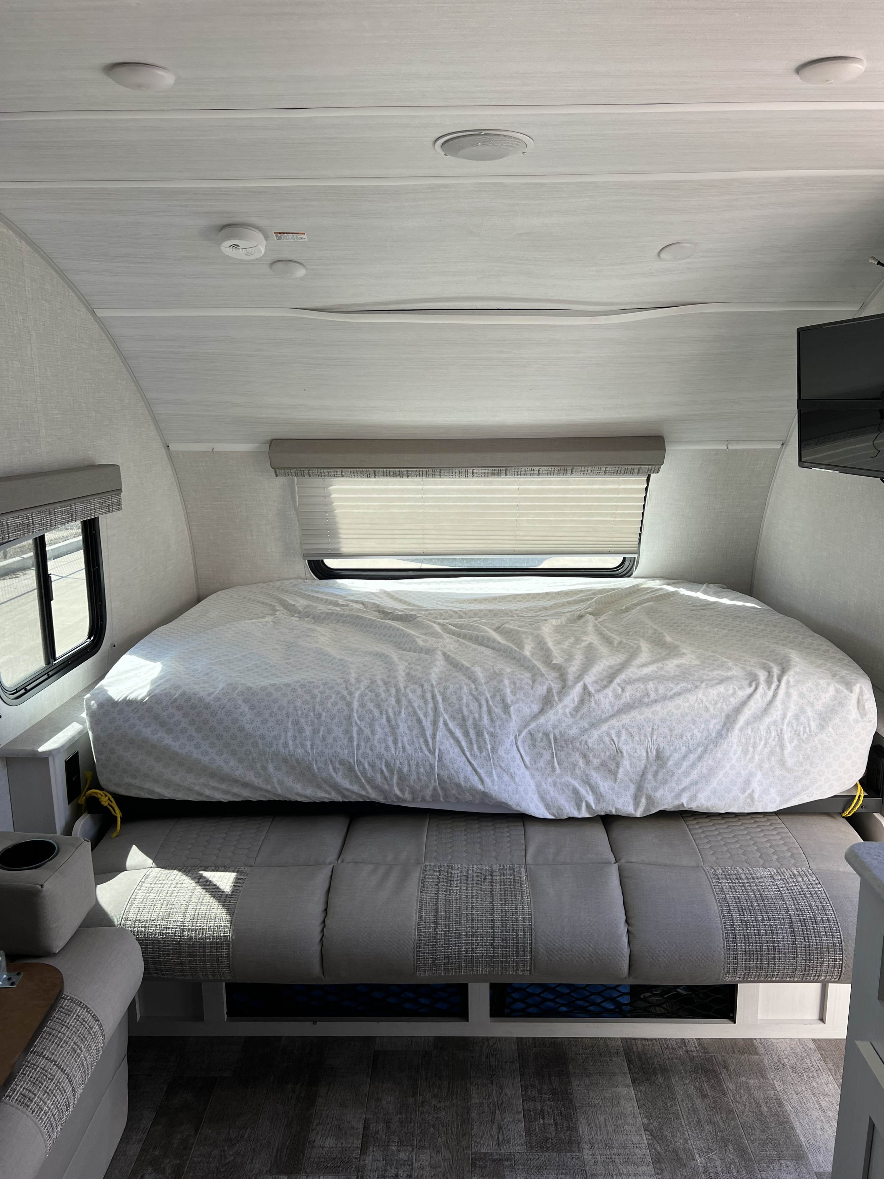 Cozy RV rental bedroom featuring a large bed with a light patterned duvet, side windows, and a convertible sofa/dinette.. Forest River R-Pod 2021