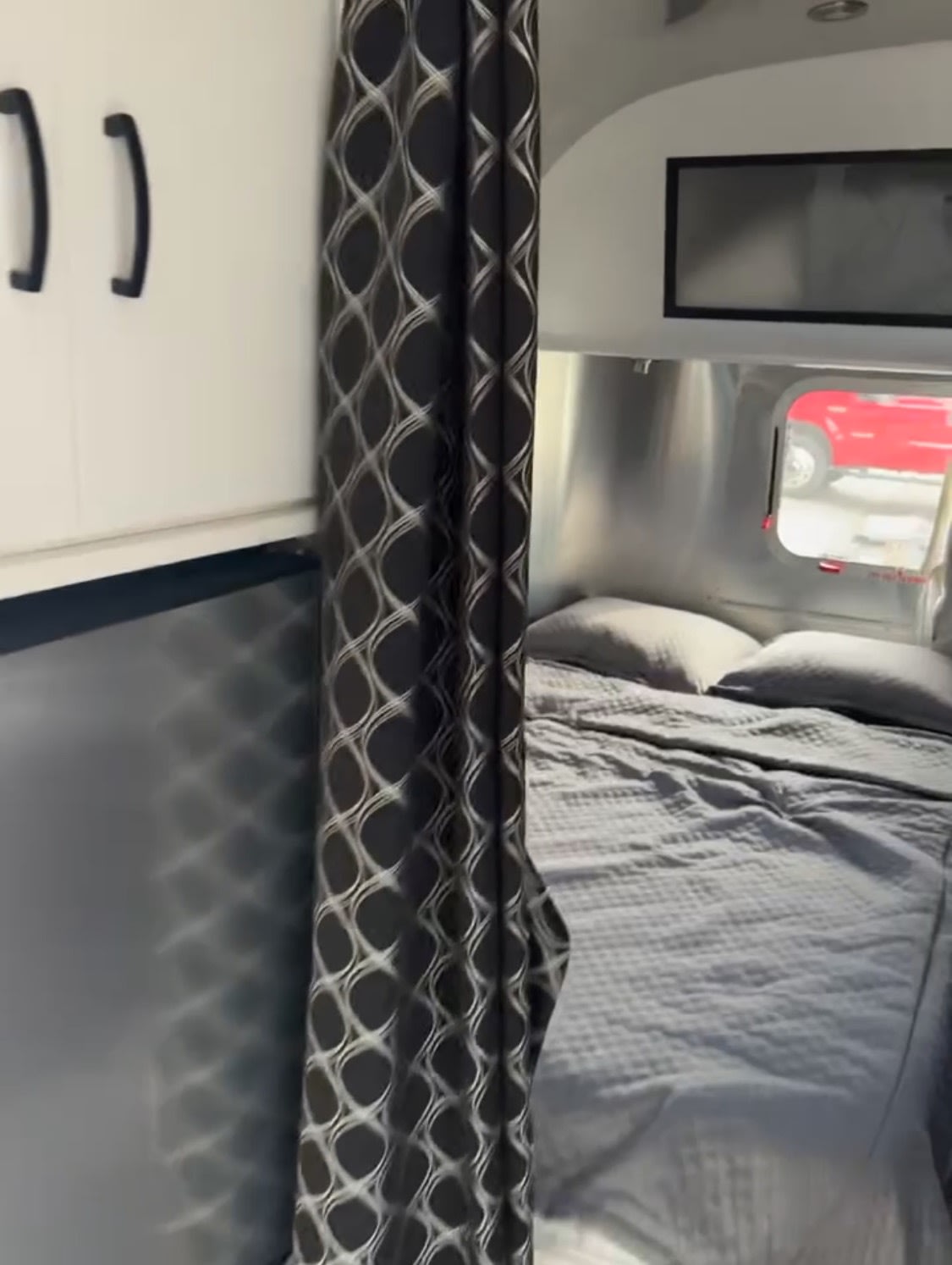 Experience comfort in this RV rental bedroom: gray bed, patterned privacy curtain, and storage cabinets for your adventure.. Airstream Caravel 2020