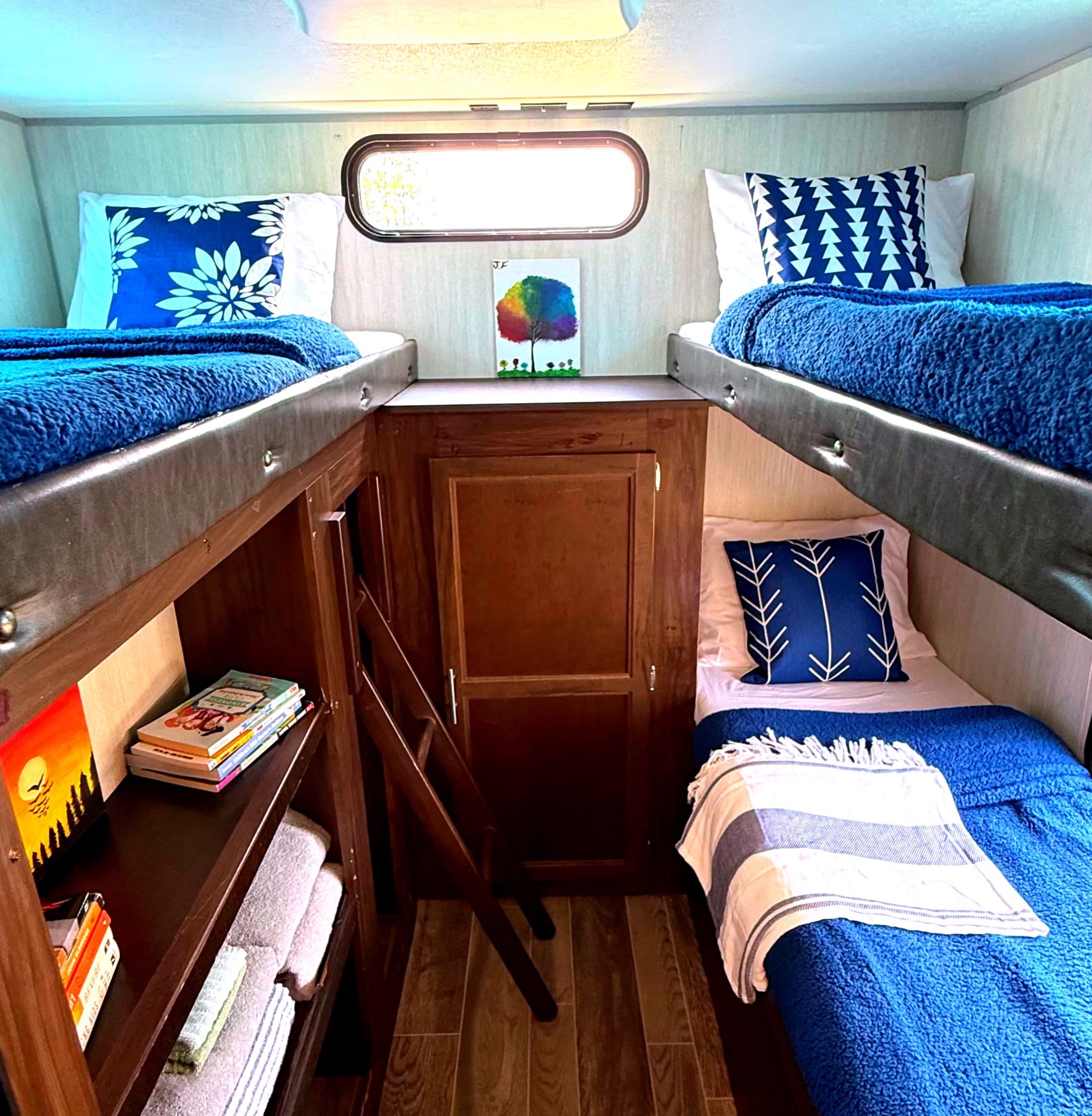 Inside an RV rental: blue bunk beds, cozy bedding, storage shelves, and a window for natural light.. Forest River Cherokee Grey Wolf 2019