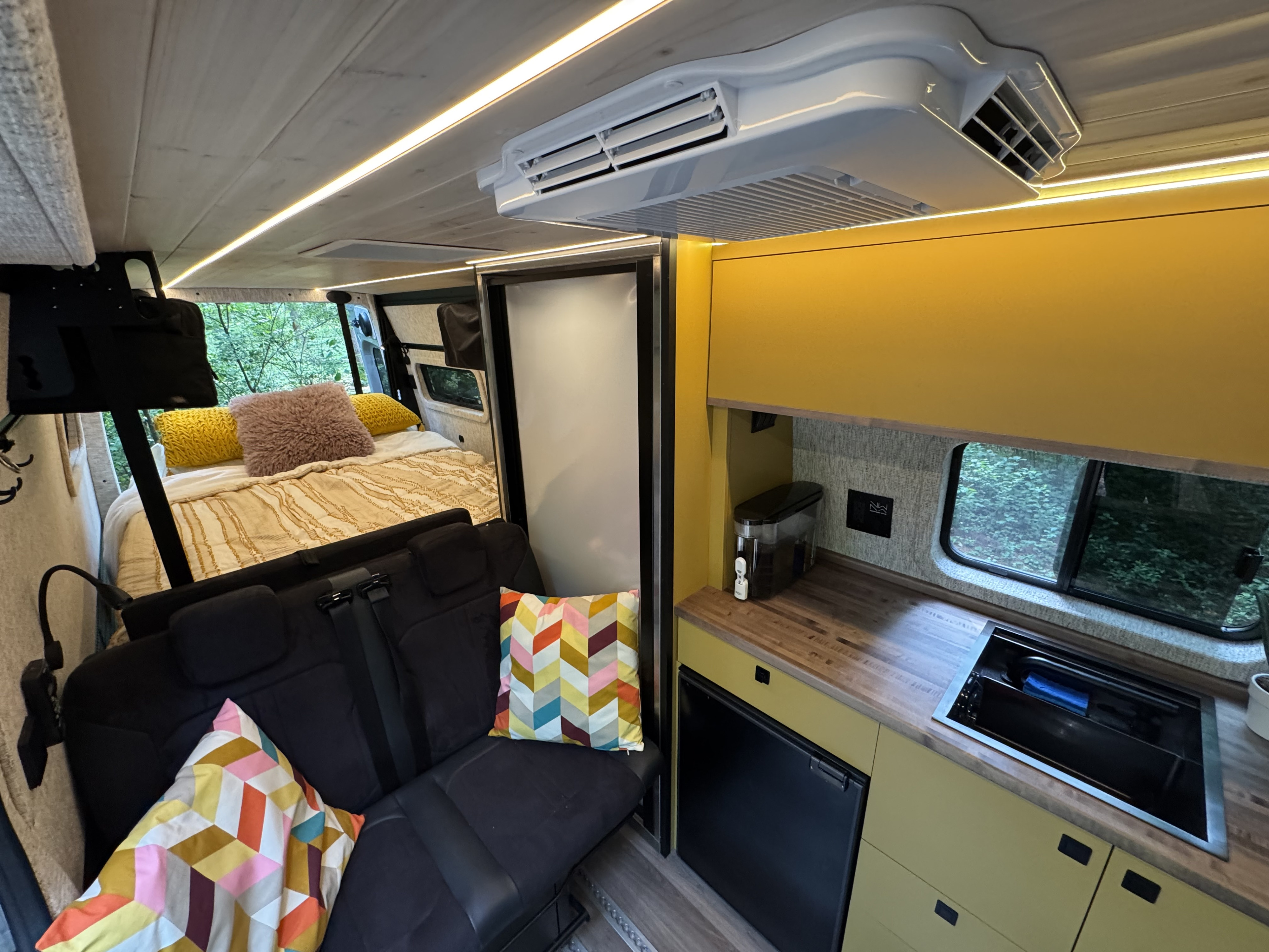 Spacious RV rental interior featuring a cozy bed, a well-equipped kitchen with sink & fridge, and a comfortable living area.. Mercedes-Benz Sprinter RV Motorhome Campervan 2022