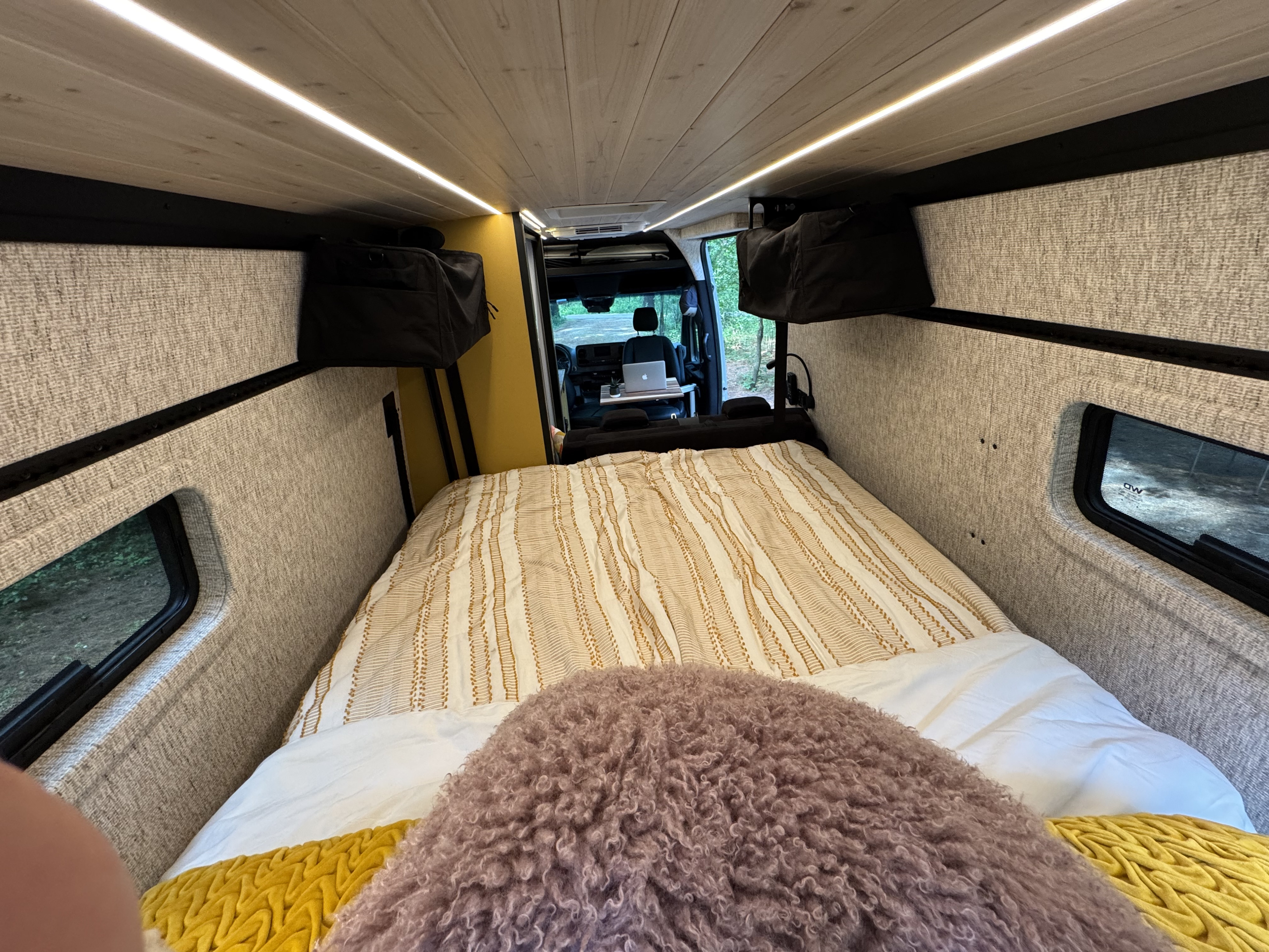 Cozy RV rental interior: Bed, desk w/ laptop, and bright lighting for comfortable van life travel.. Mercedes-Benz Sprinter RV Motorhome Campervan 2022