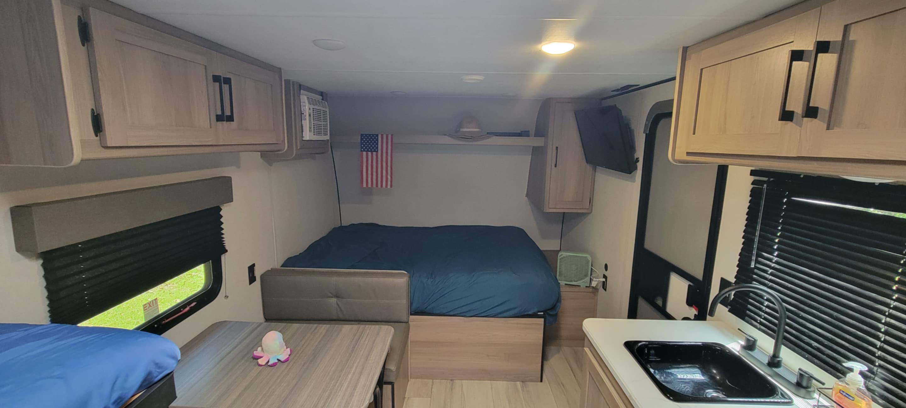 Inside an rv rental: a compact living space featuring a comfortable bed, dinette, kitchen sink, and overhead cabinets.. Keystone Coleman 17b 2025
